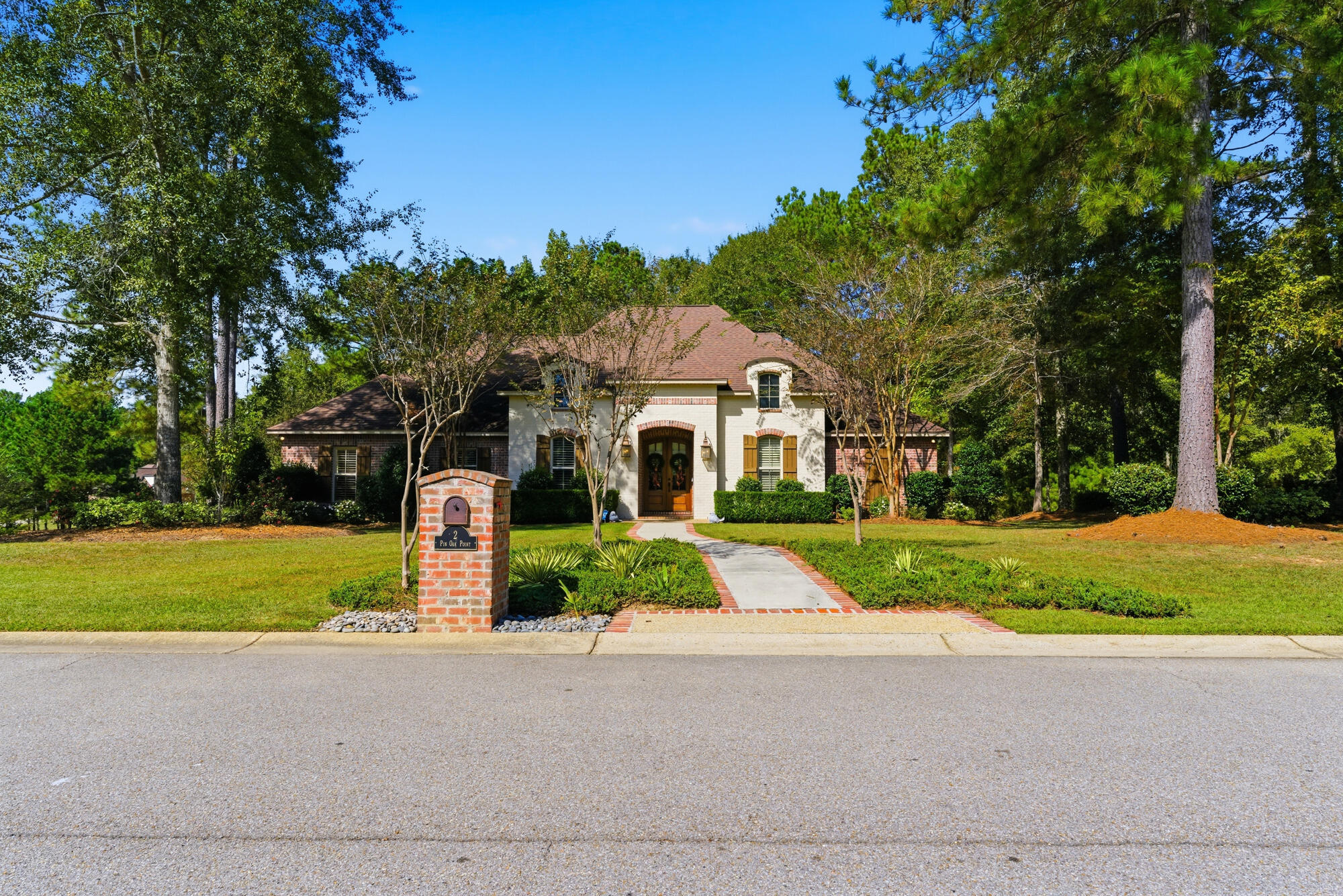 Cream stucco and brick home with an arched entry, brick walkway, and mature trees.