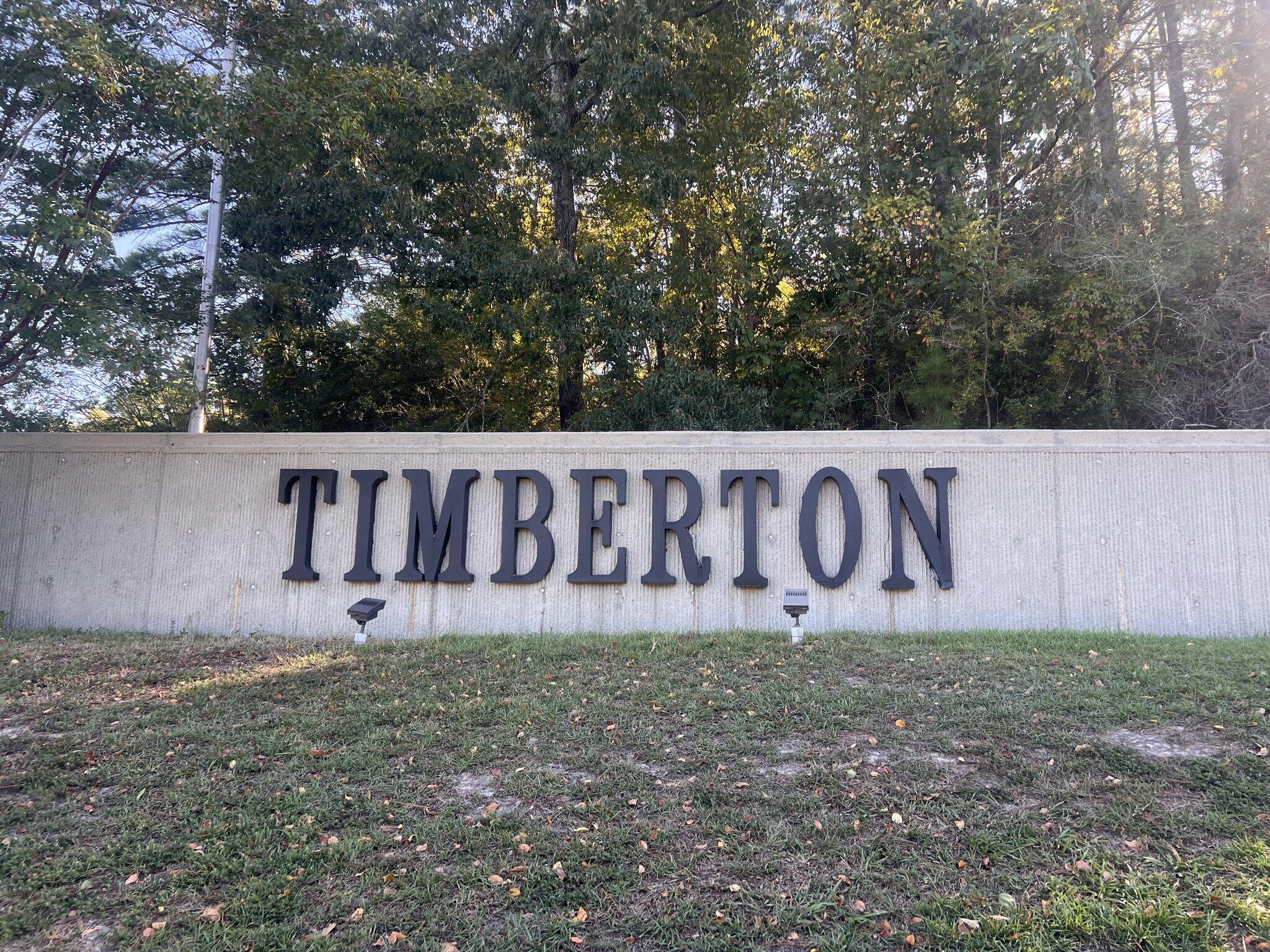 Timberton neighborhood entrance sign on a concrete wall beneath trees.