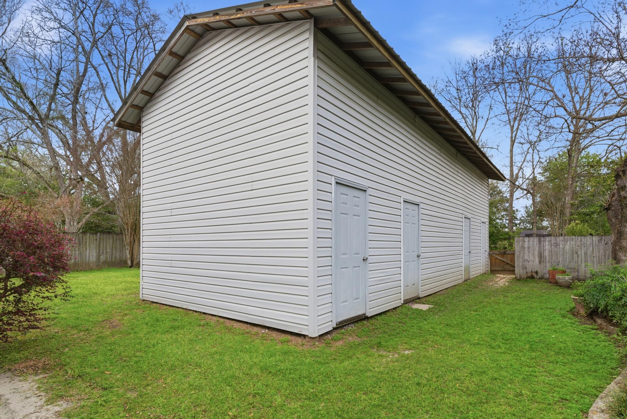 White-sided outbuilding with multiple gray doors beside a fenced grassy yard.