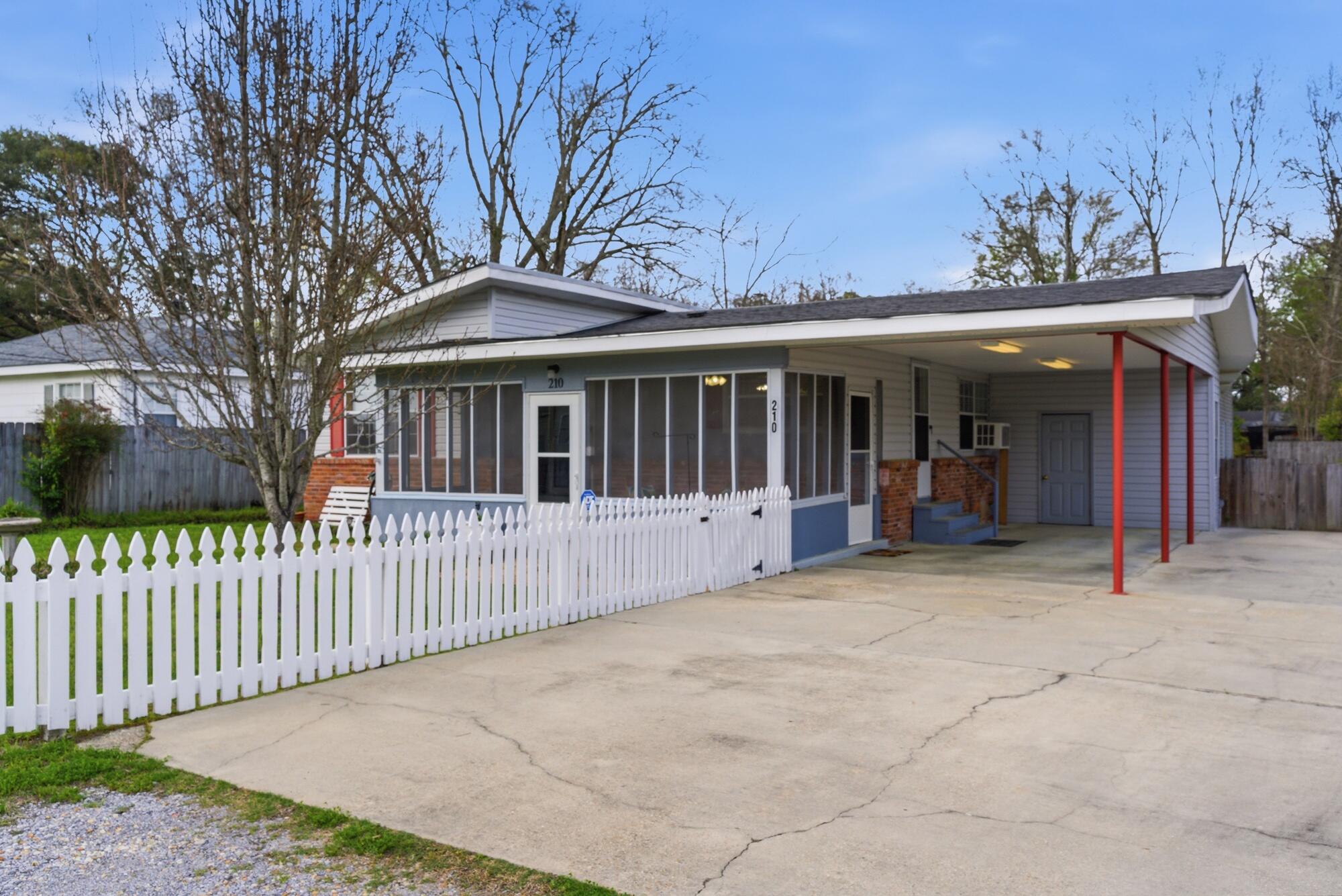 House with a screened front porch, white picket fence, and red-post carport.