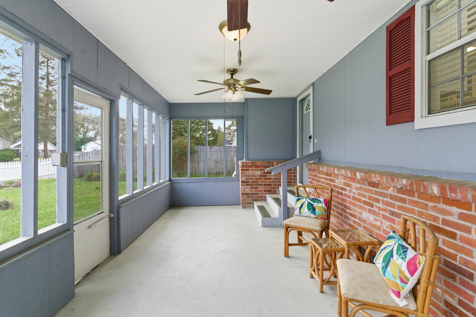 Enclosed porch with screened windows, a brick half-wall, ceiling fans, and wicker seating with colorful cushions.