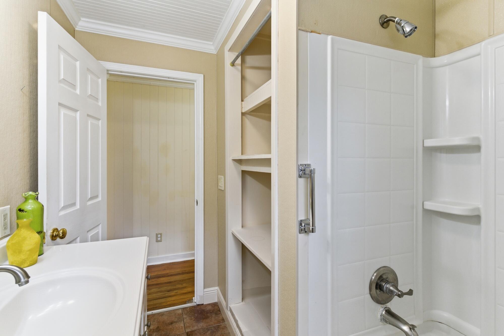 Bathroom with a white tiled shower, open built-in shelves, and a vanity topped with colorful vases.
