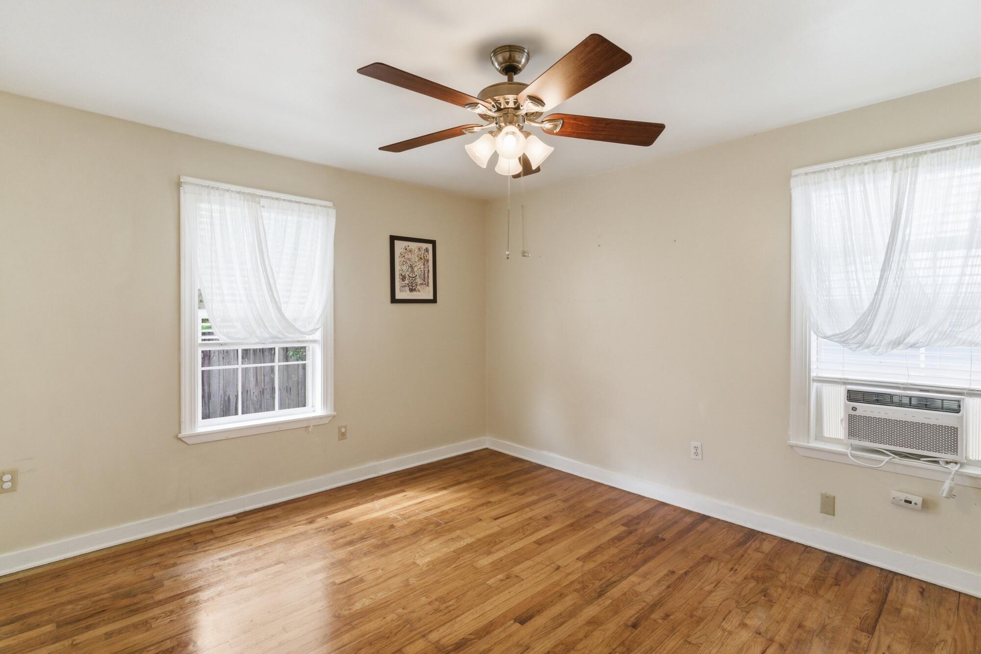 Empty room with hardwood floors, two curtained windows, and a ceiling fan with lights.