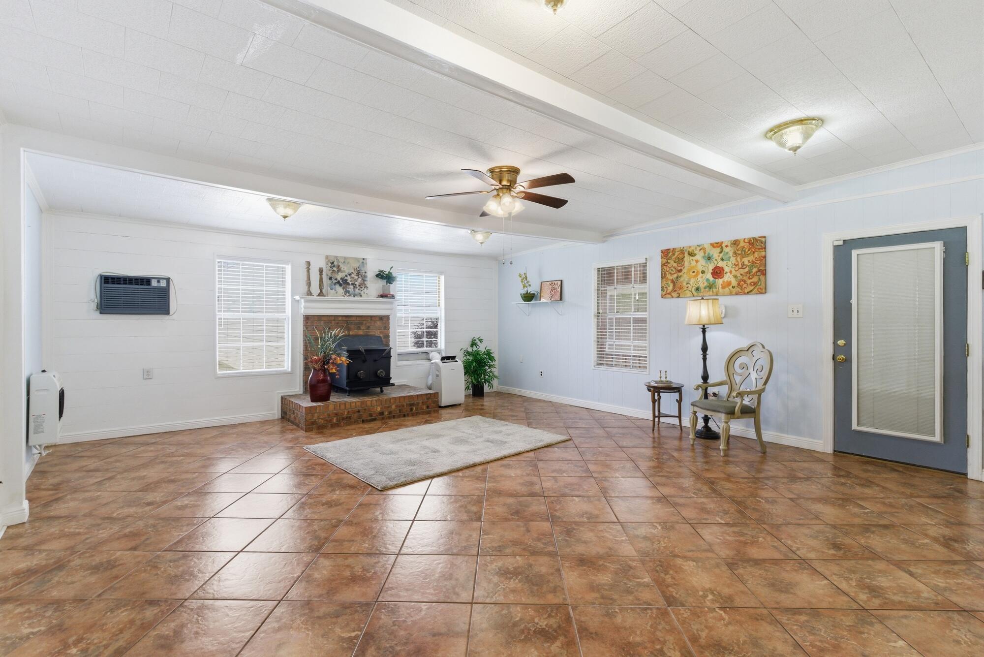 Living room with terracotta tile floors, a raised brick hearth, and a ceiling fan.