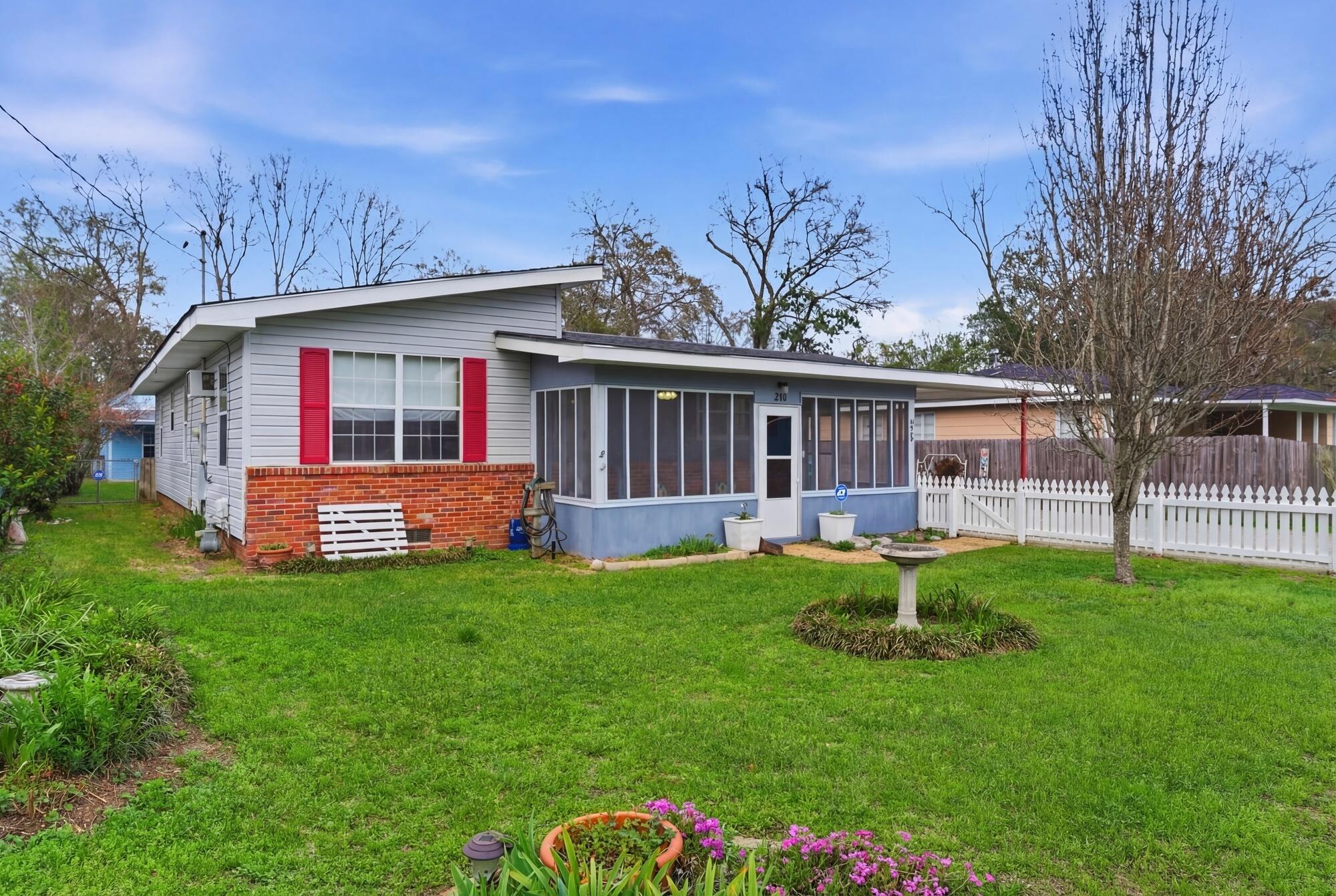Single-story home with red shutters, a screened porch, and a white picket fence.