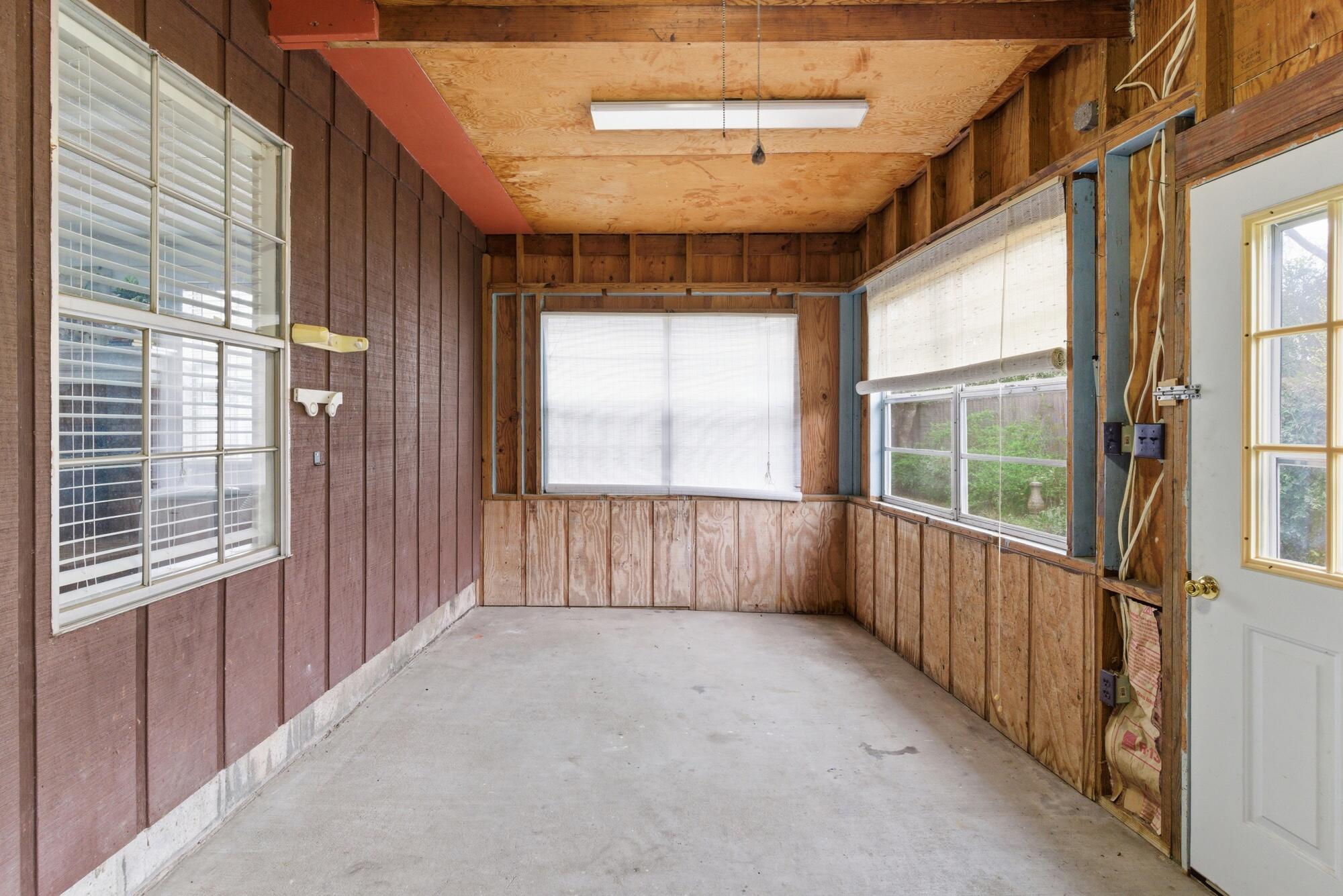 Unfinished enclosed porch with exposed wood walls, a concrete floor, and windows with blinds.