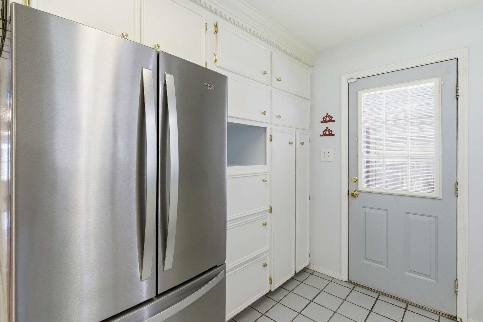 Kitchen with a stainless steel refrigerator, white cabinetry, tiled floor, and a gray door with window blinds.
