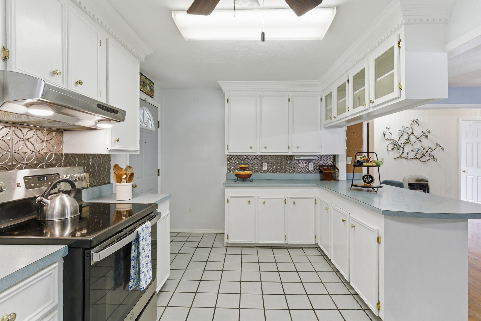 Kitchen with white cabinets, a blue peninsula counter, patterned backsplash, and stainless steel range.