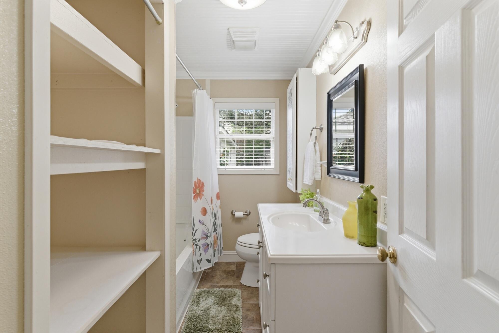 Bathroom with built-in shelves, a white vanity, and a floral shower curtain.