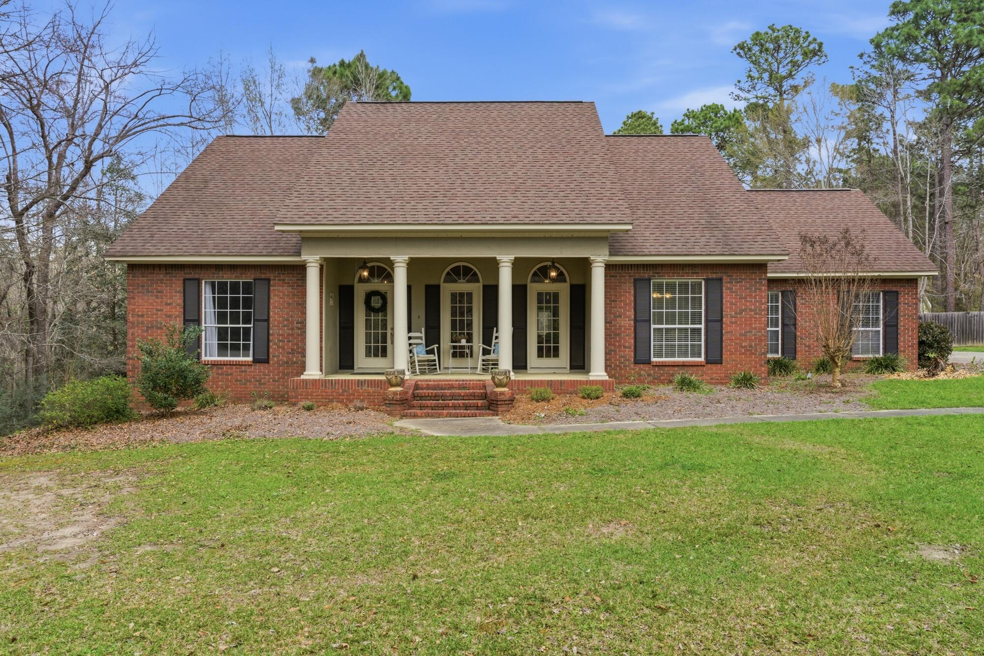 Red brick home with a wide covered porch, white columns, rocking chairs, and a broad front lawn.