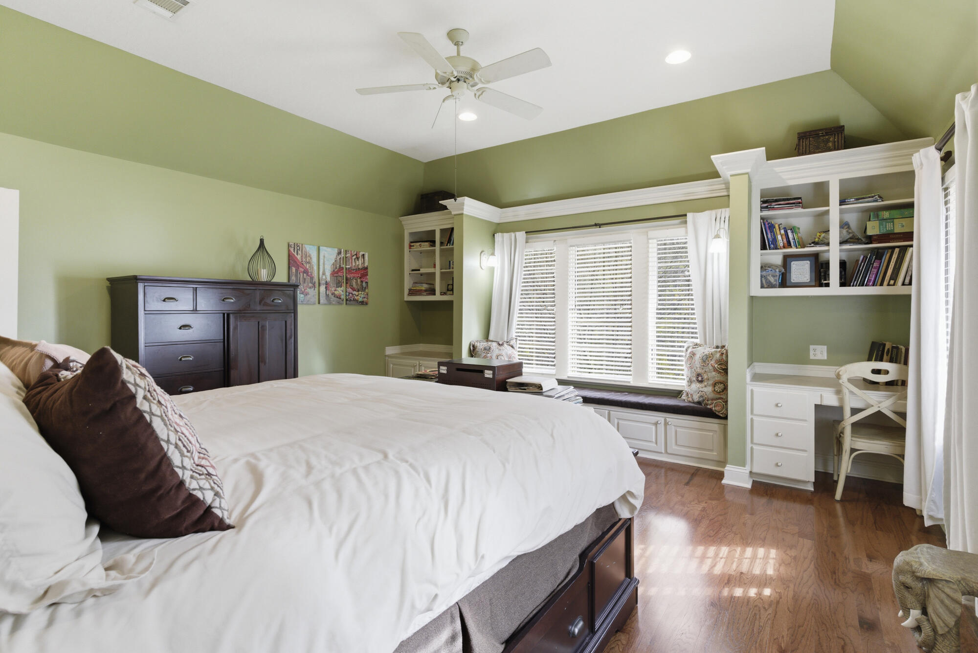 Bedroom with a large bed, sage-green walls, built-in bookshelves, and a window seat.