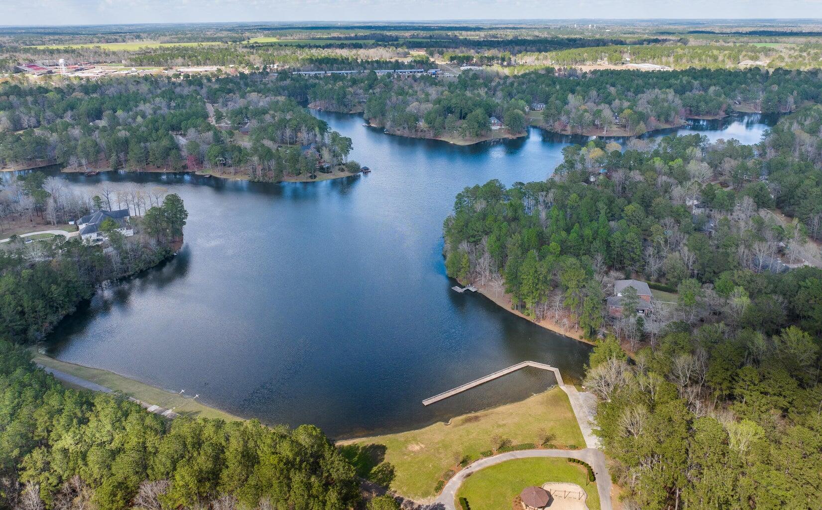 Aerial view of a wooded lake with waterfront homes, docks, and a grassy recreation area.
