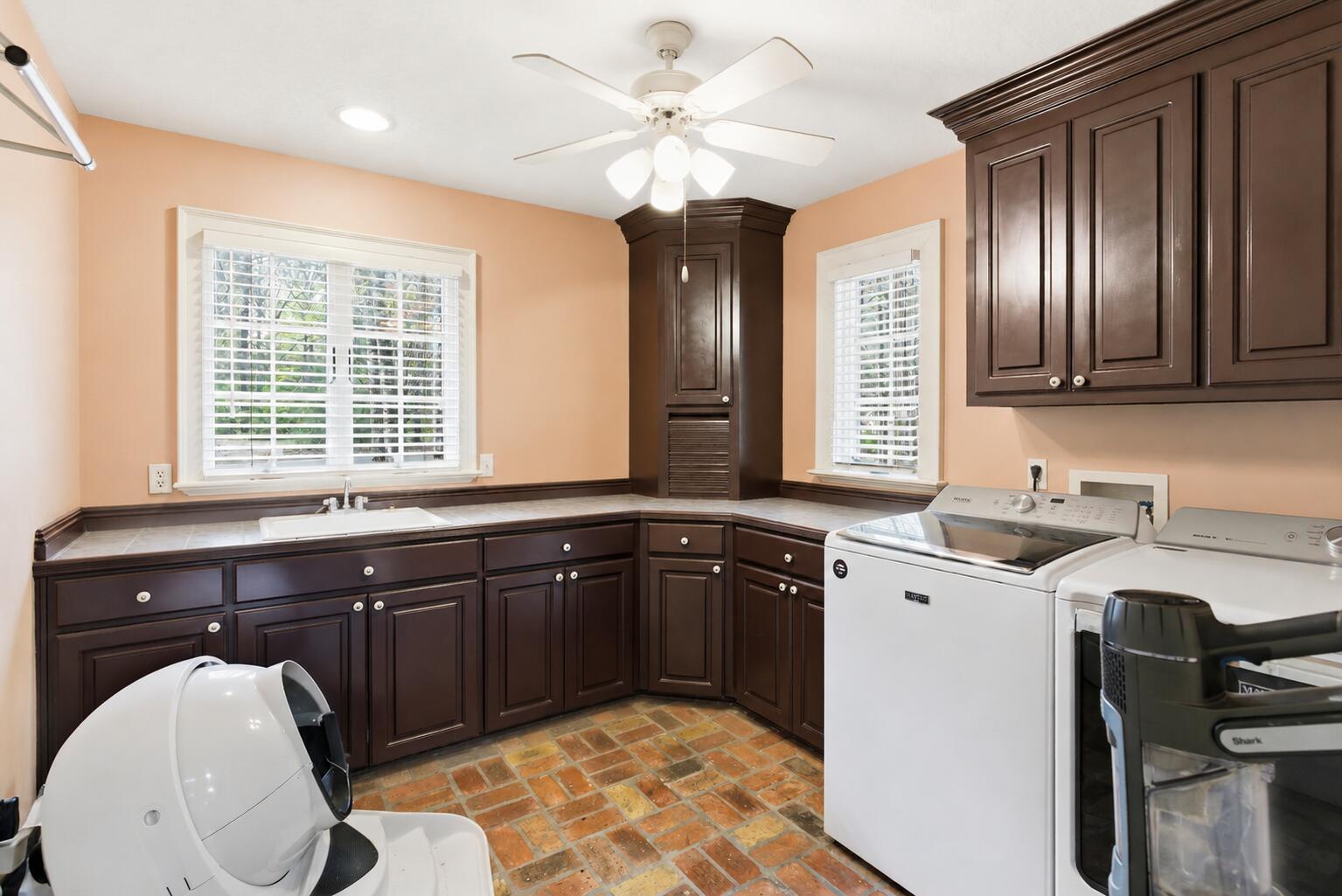 Laundry room with dark wood cabinetry, brick flooring, and white washer and dryer.