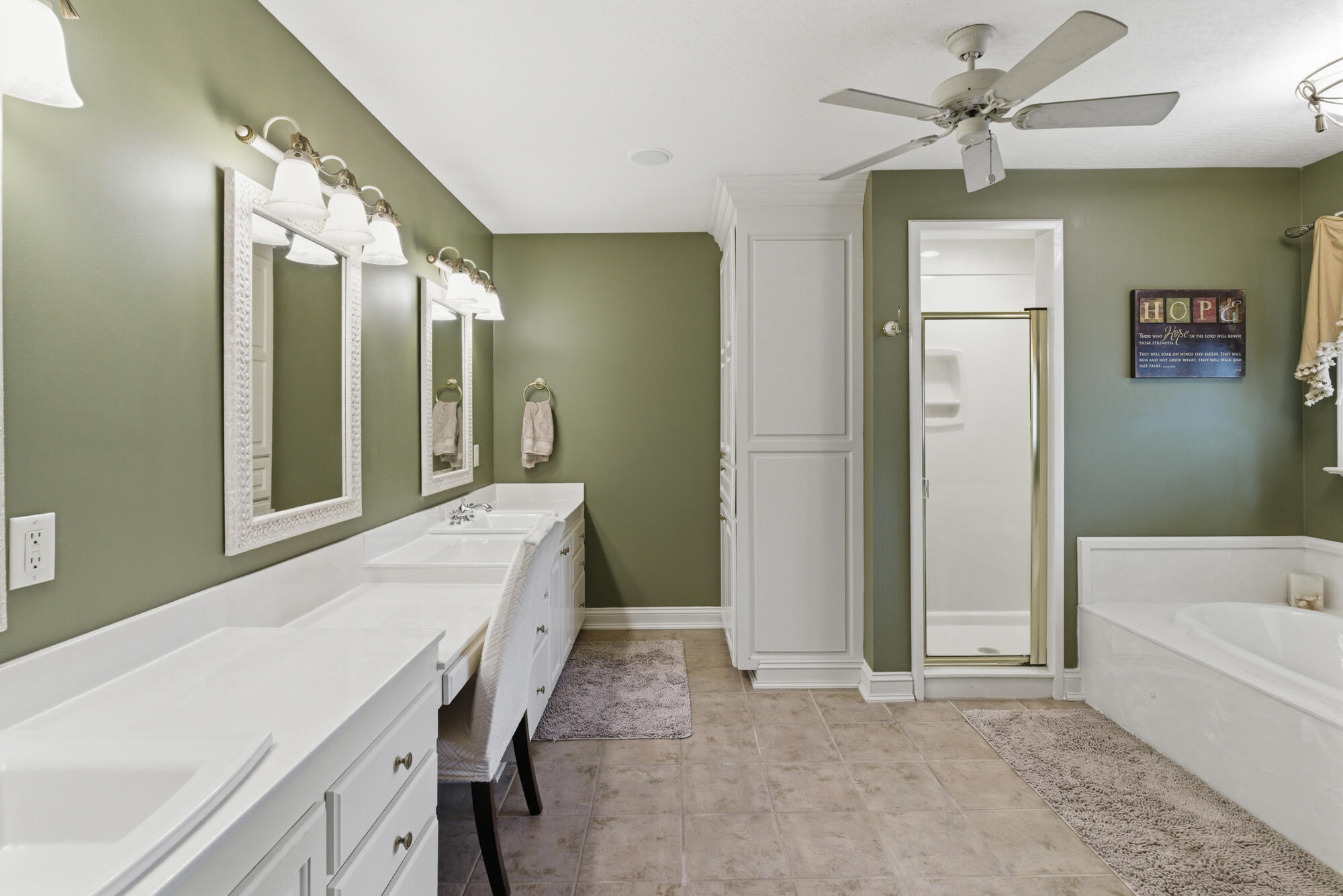 Bathroom with a long double vanity, olive-green walls, glass shower, and white soaking tub.