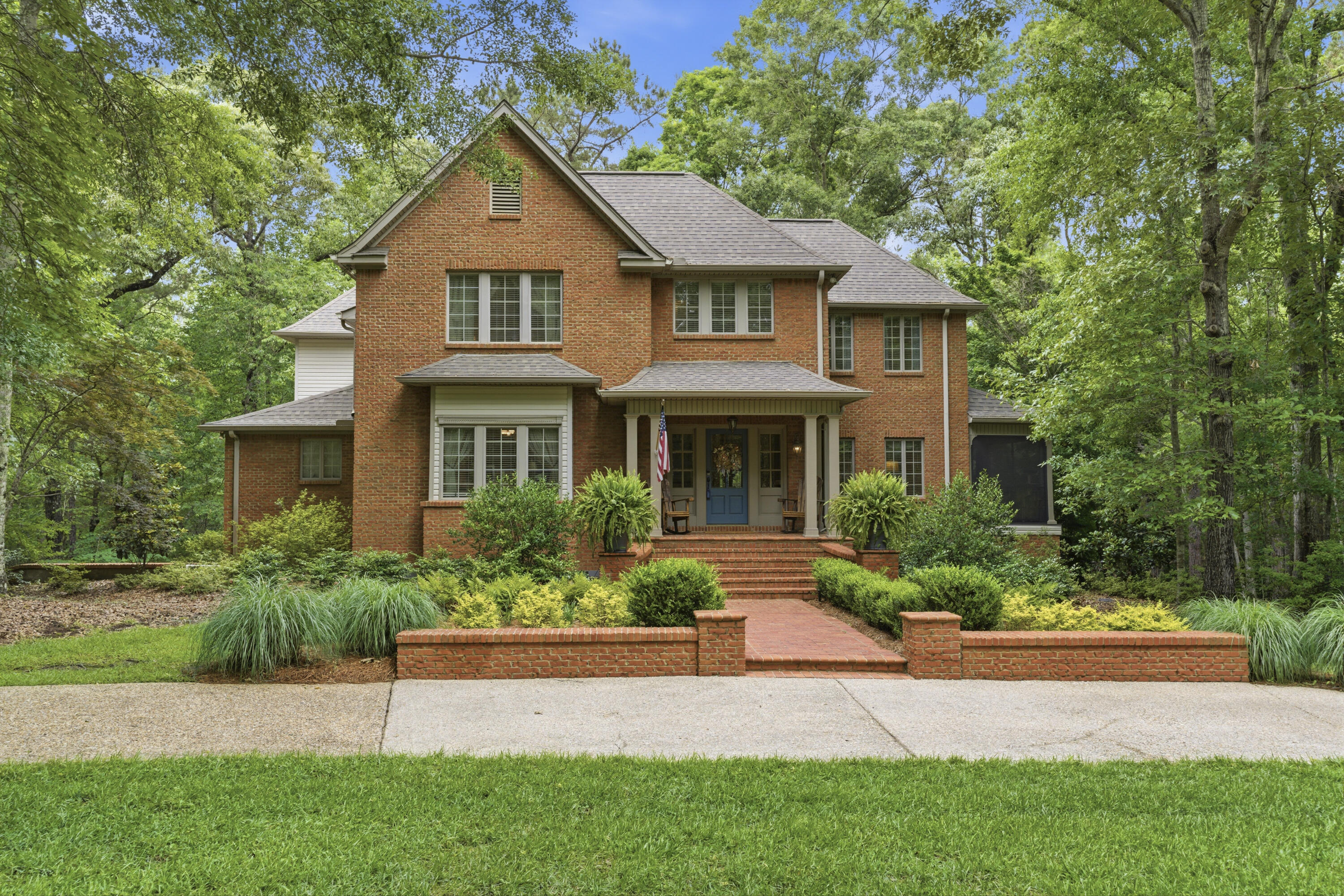Two-story brick house with a blue front door, covered porch, and landscaped brick walkway.