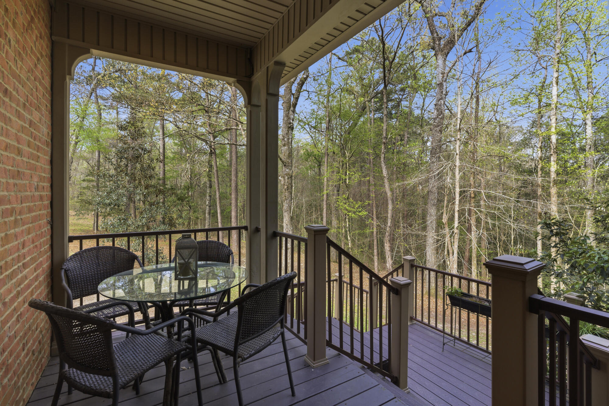 Covered deck with wicker seating and glass table overlooking a wooded yard.