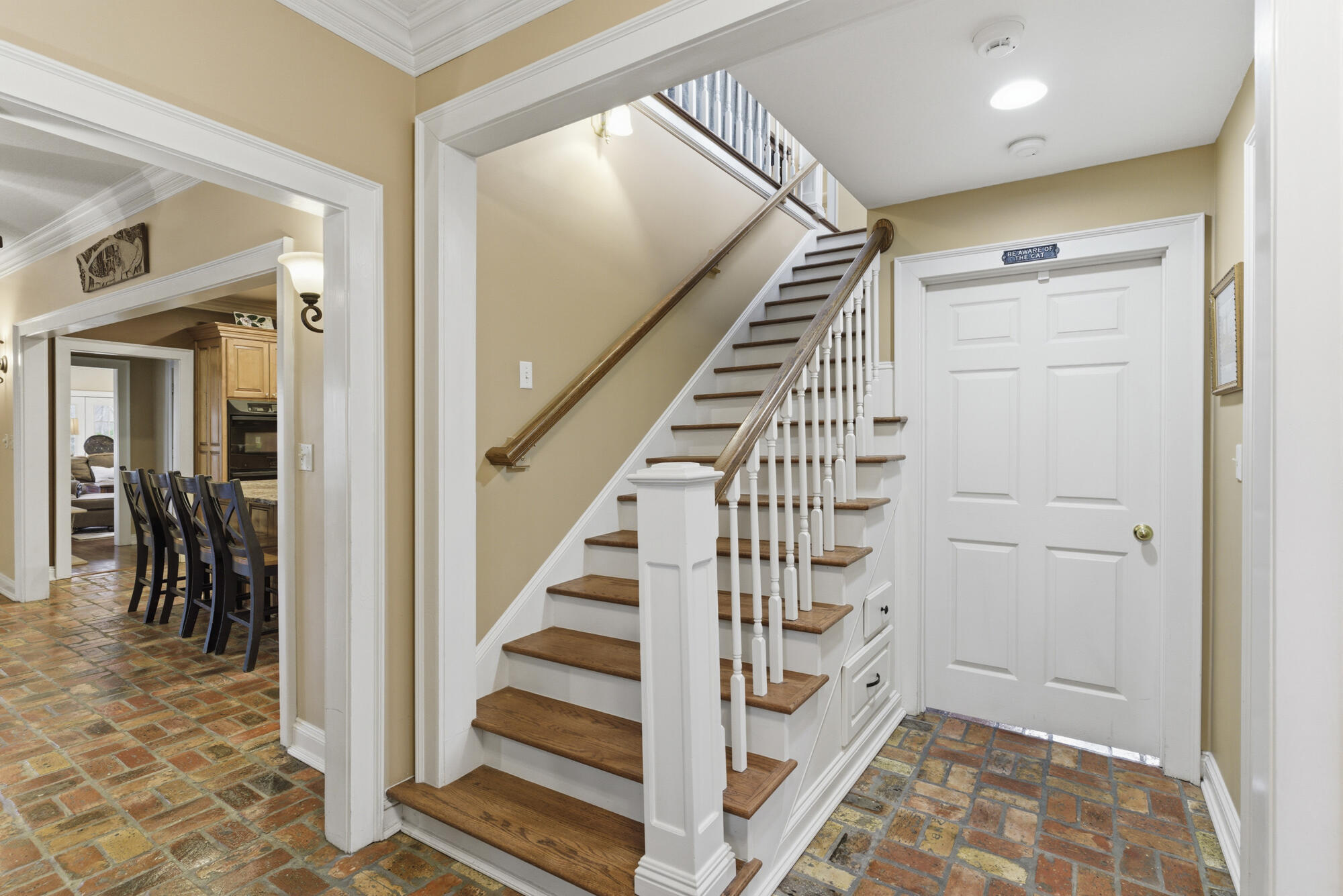 Foyer staircase with wood treads and railing, brick flooring, and an adjoining dining area.