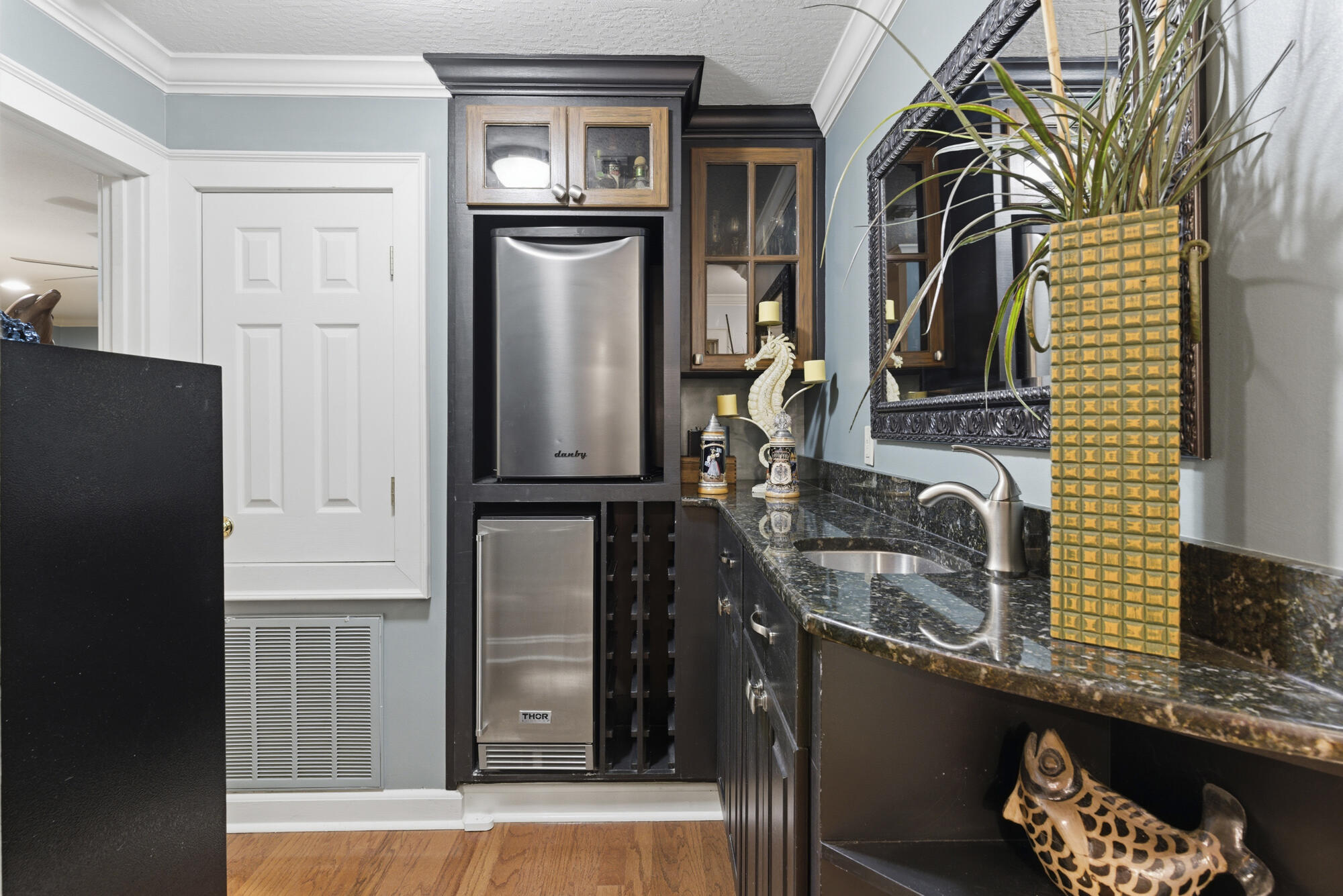 Wet bar with stainless beverage refrigerators, a small sink, dark granite counters, and a built-in wine rack.