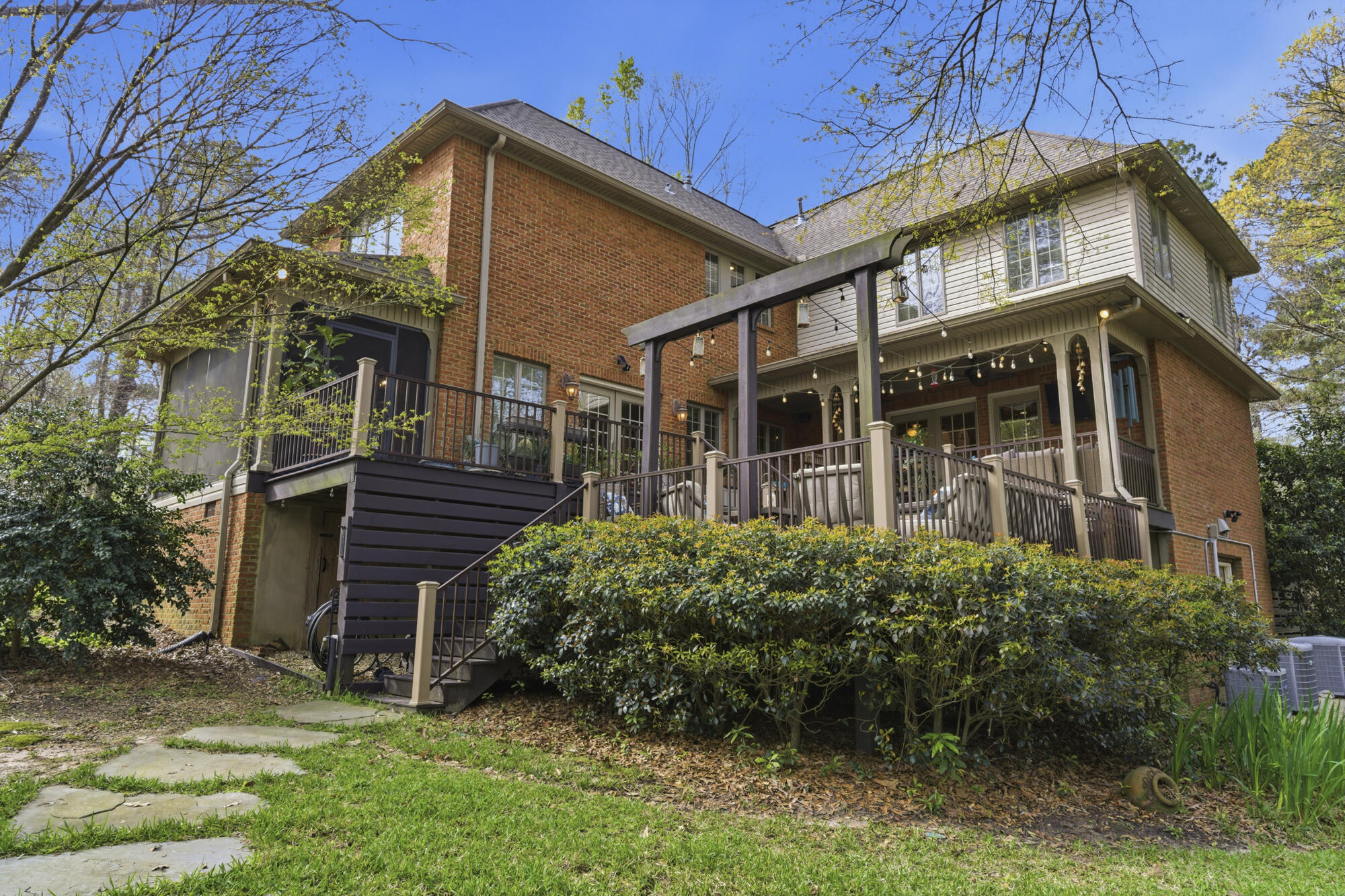 Rear of a two-story home with a raised deck, screened porch, pergola, and landscaped yard.