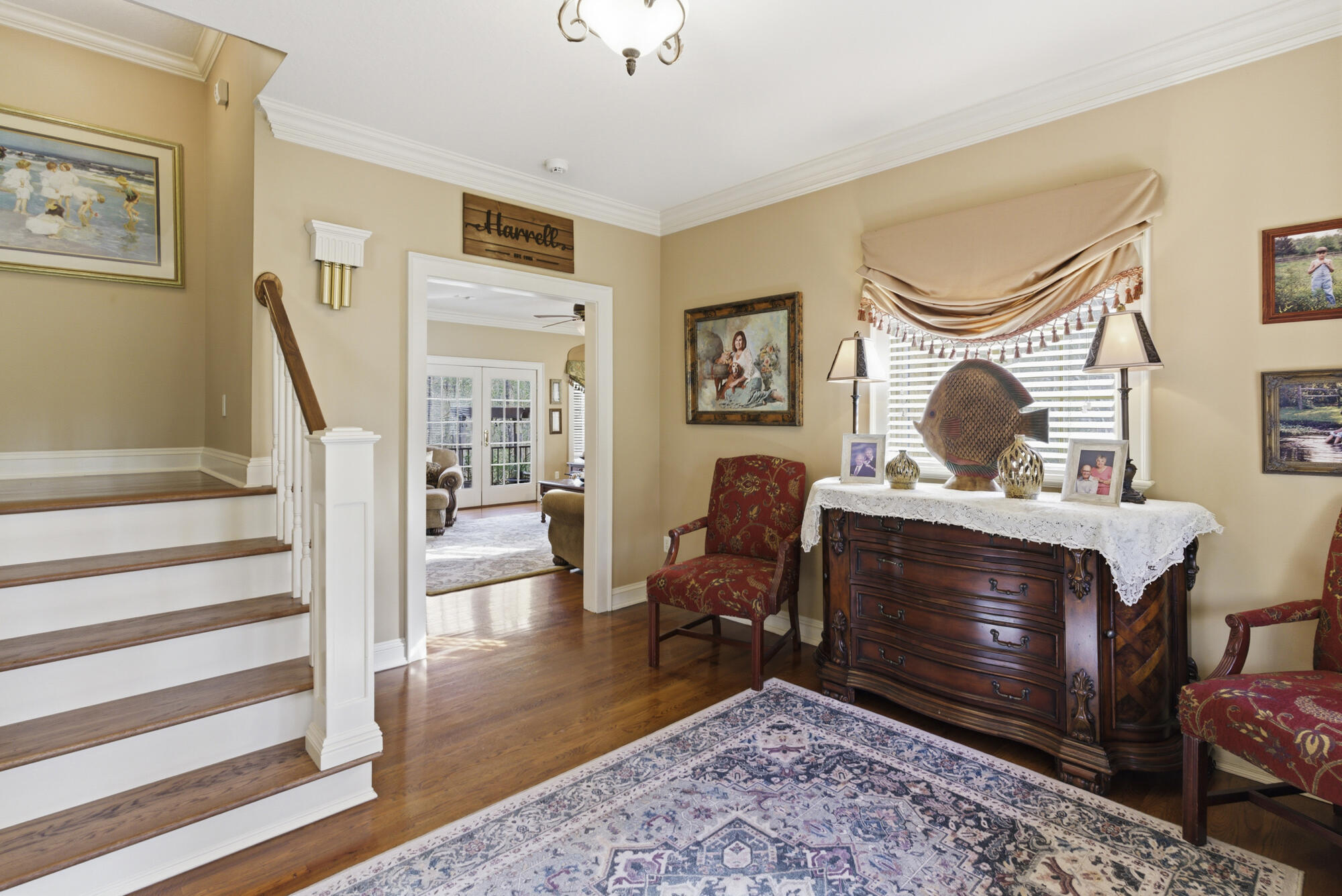 Foyer with a wood staircase, patterned rug, and ornate dresser beneath a curtained window.
