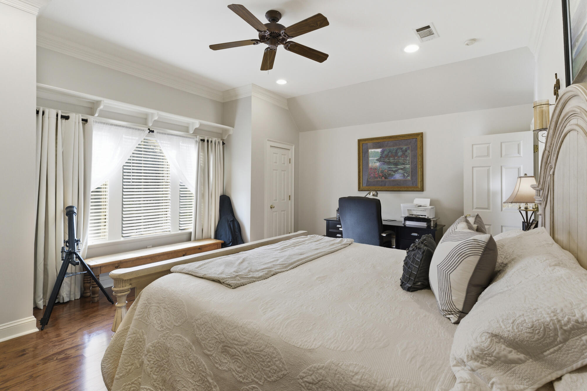 Bedroom with a large bed, hardwood floors, and a desk beside the window.