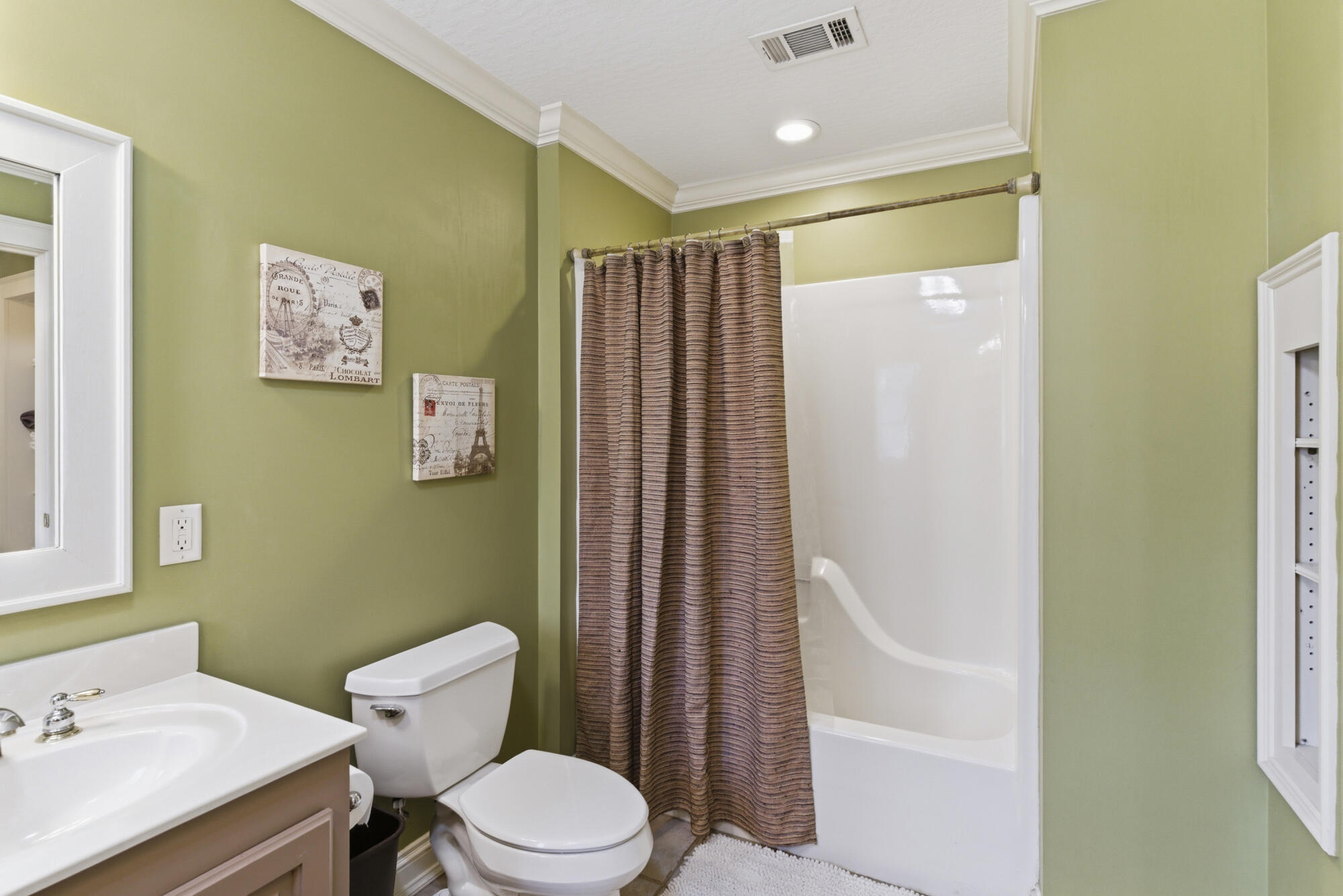 Bathroom with olive-green walls, a white tub-shower, and a brown striped curtain.