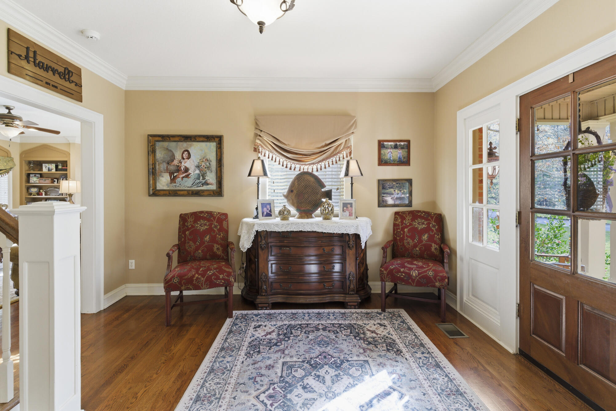 Entry sitting area with a dark wood chest, red armchairs, patterned rug, and glass-paneled front door.