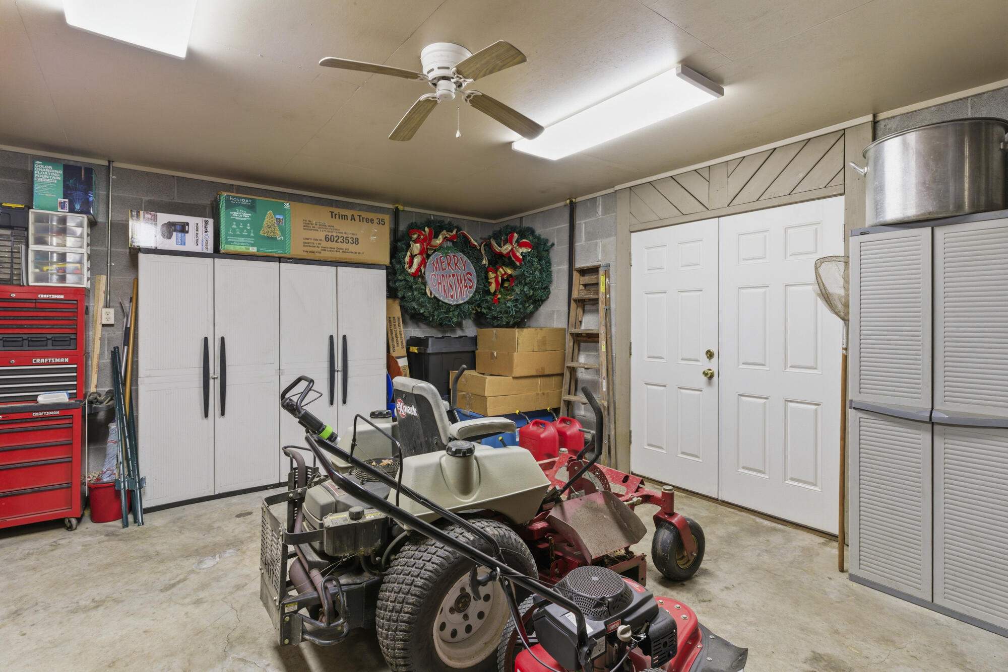 Garage with lawn mowers, storage cabinets, and a Christmas wreath above stacked boxes.