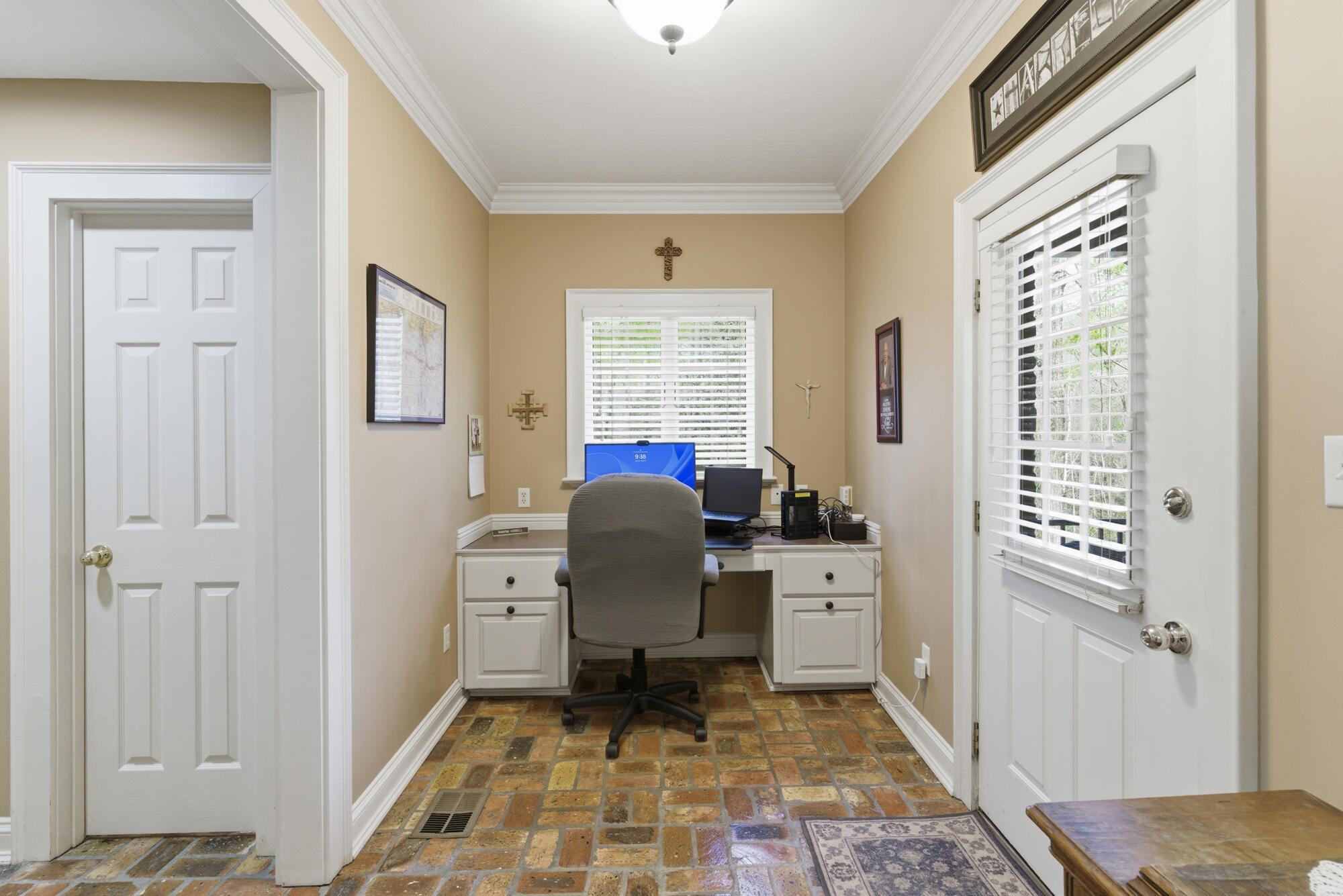 Home office with a built-in desk, computer, gray chair, and brick tile floor.