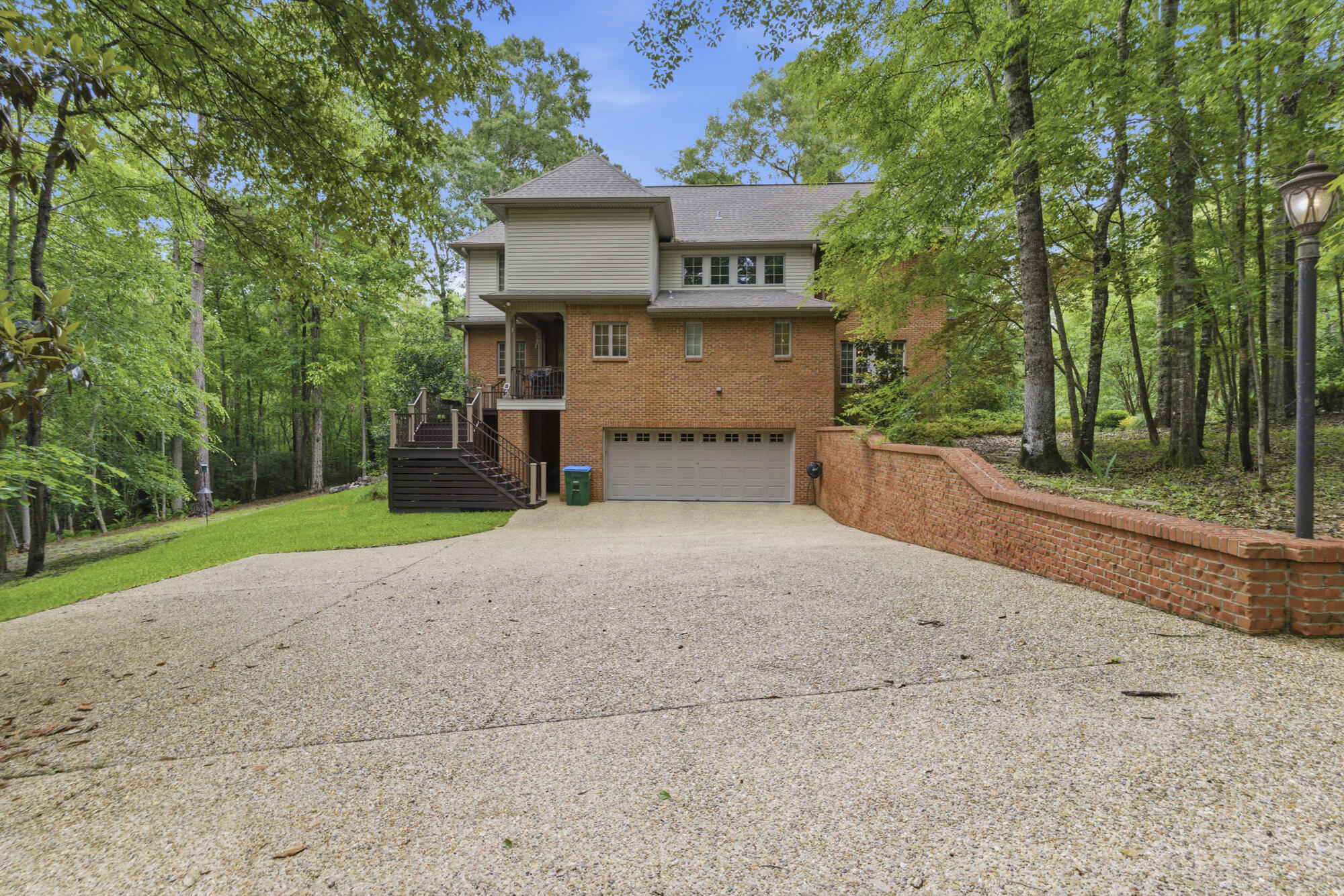 Two-story brick-and-siding home with a double garage, raised deck, and wooded surroundings.