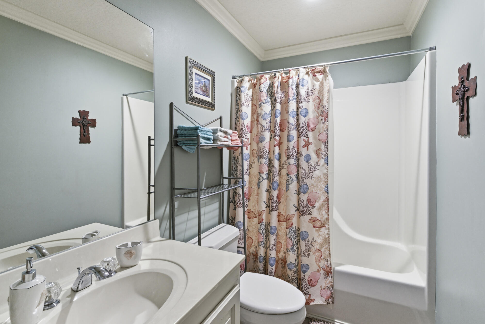 Bathroom with a white vanity and tub, seashell-patterned shower curtain, and folded towels.