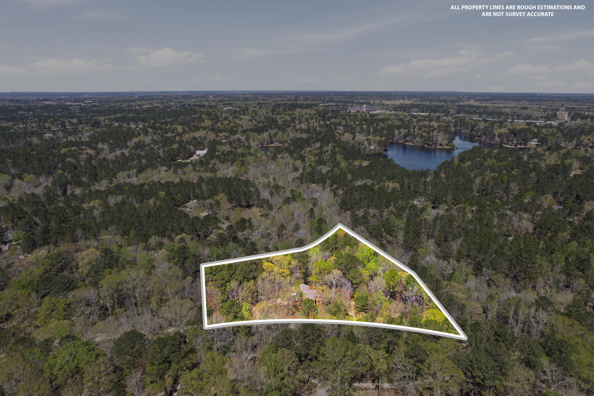 Aerial view of a wooded property outlined in white, with a house among the trees and water in the distance.