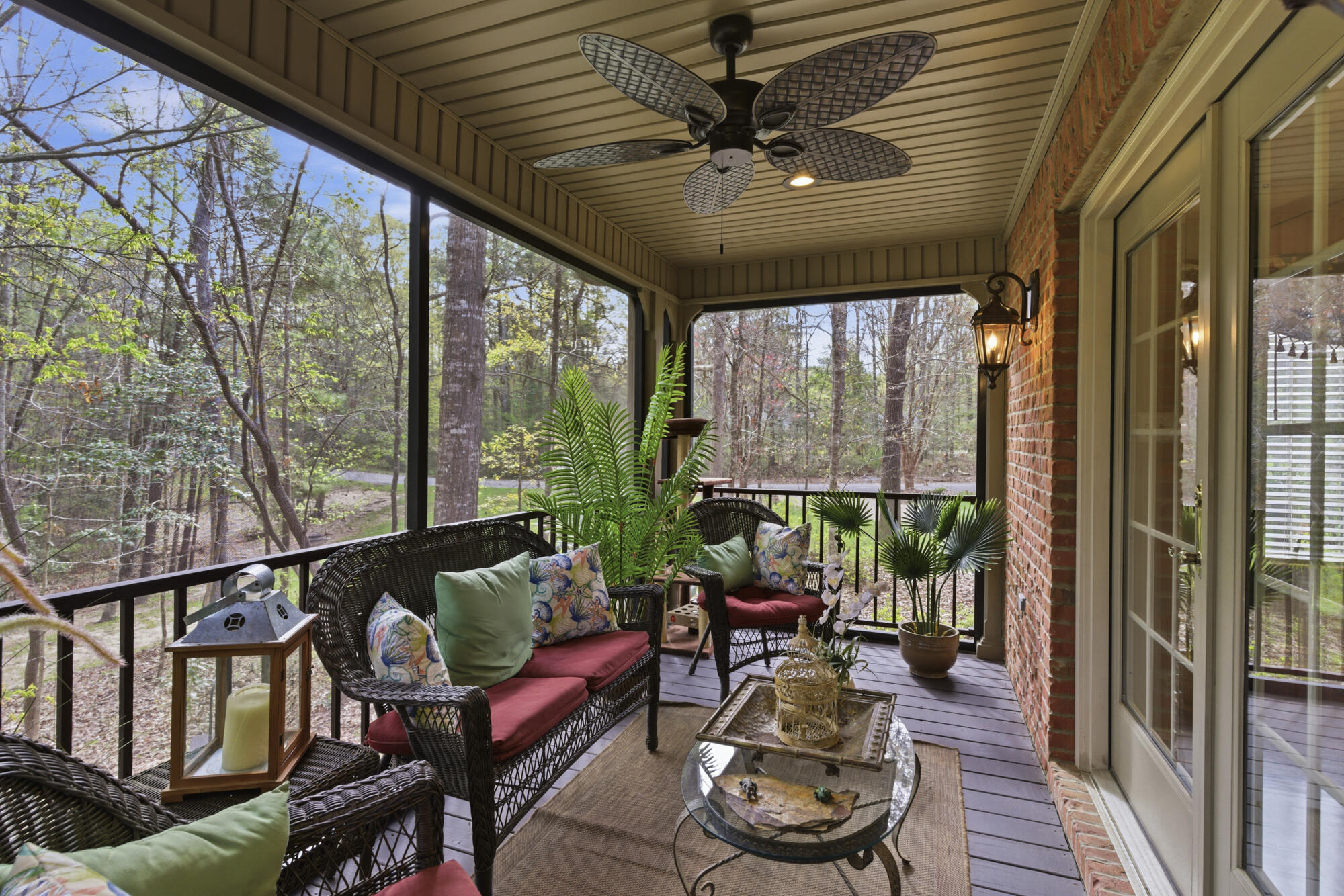 Covered porch with wicker seating and red cushions overlooking a wooded yard.
