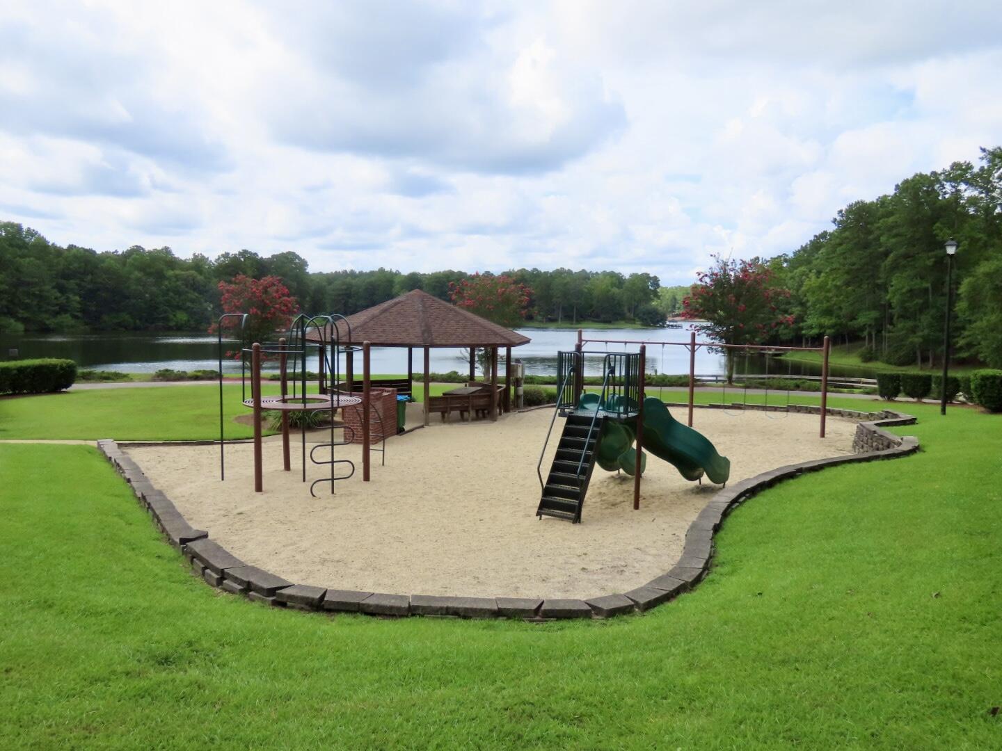 Community playground with a gazebo and climbing equipment beside a lake.