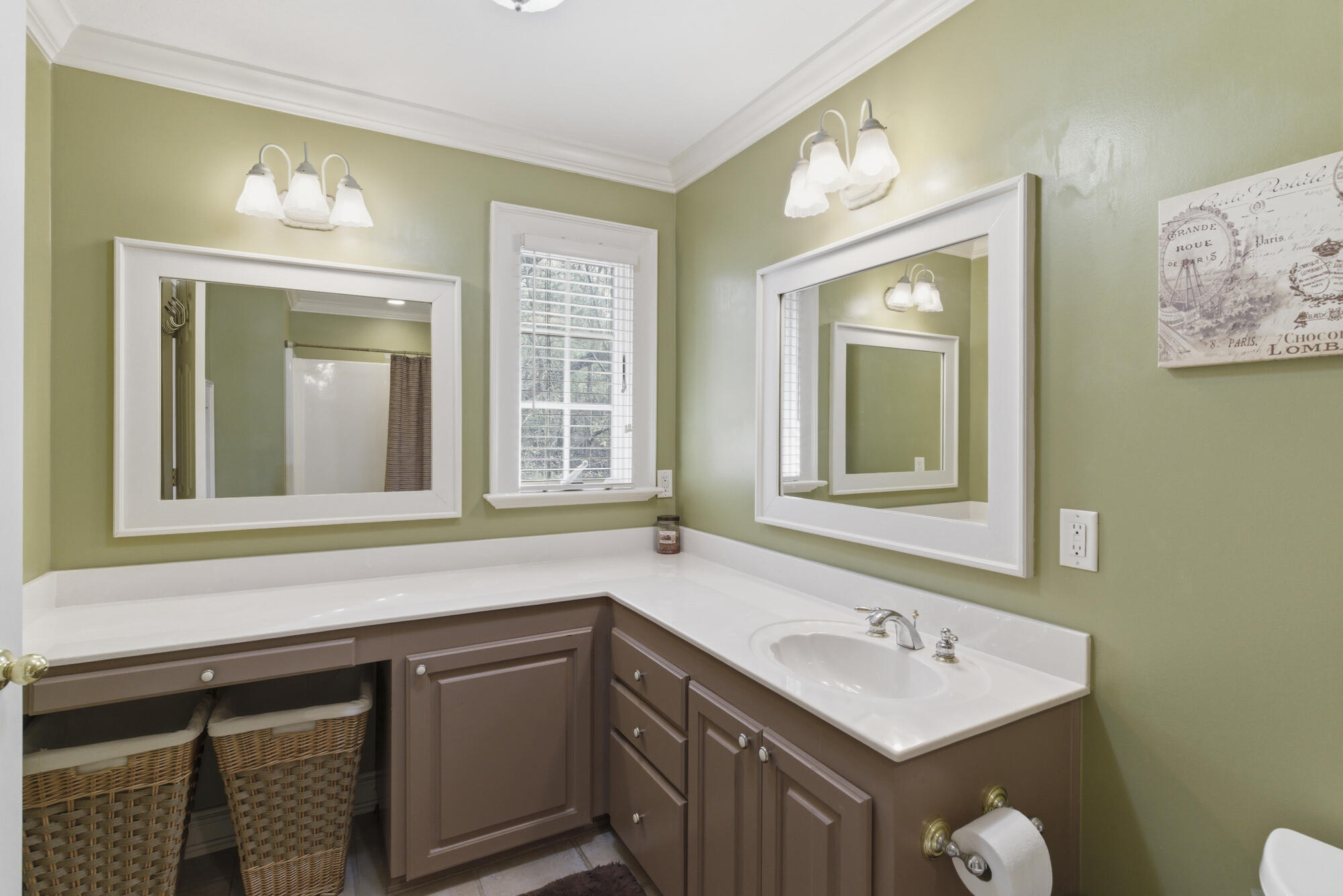 Bathroom vanity with brown cabinets, a white sink, two large mirrors, and green walls.