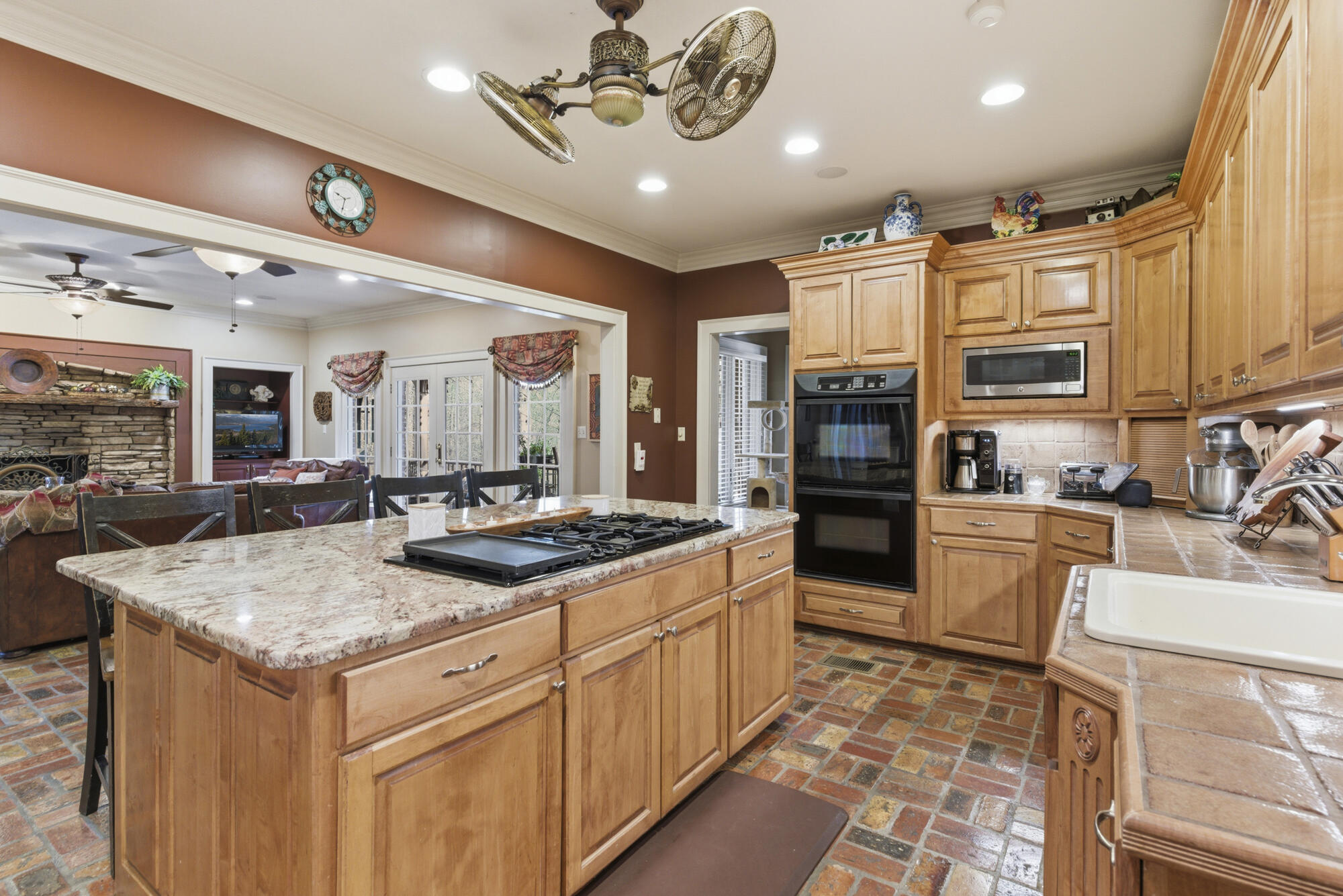 Kitchen with a granite island and gas cooktop, wood cabinetry, double oven, and brick flooring.