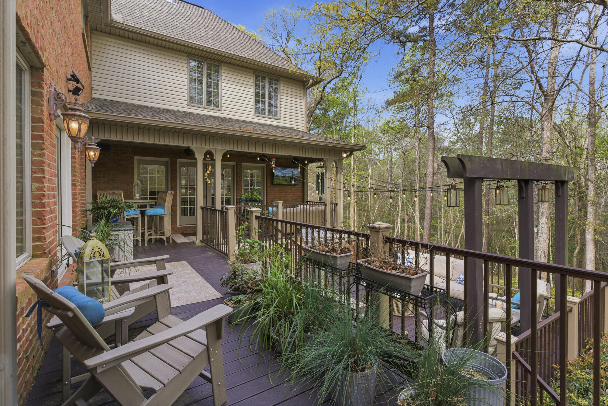Raised deck with patio seating, planters, string lights, and a wooded view.