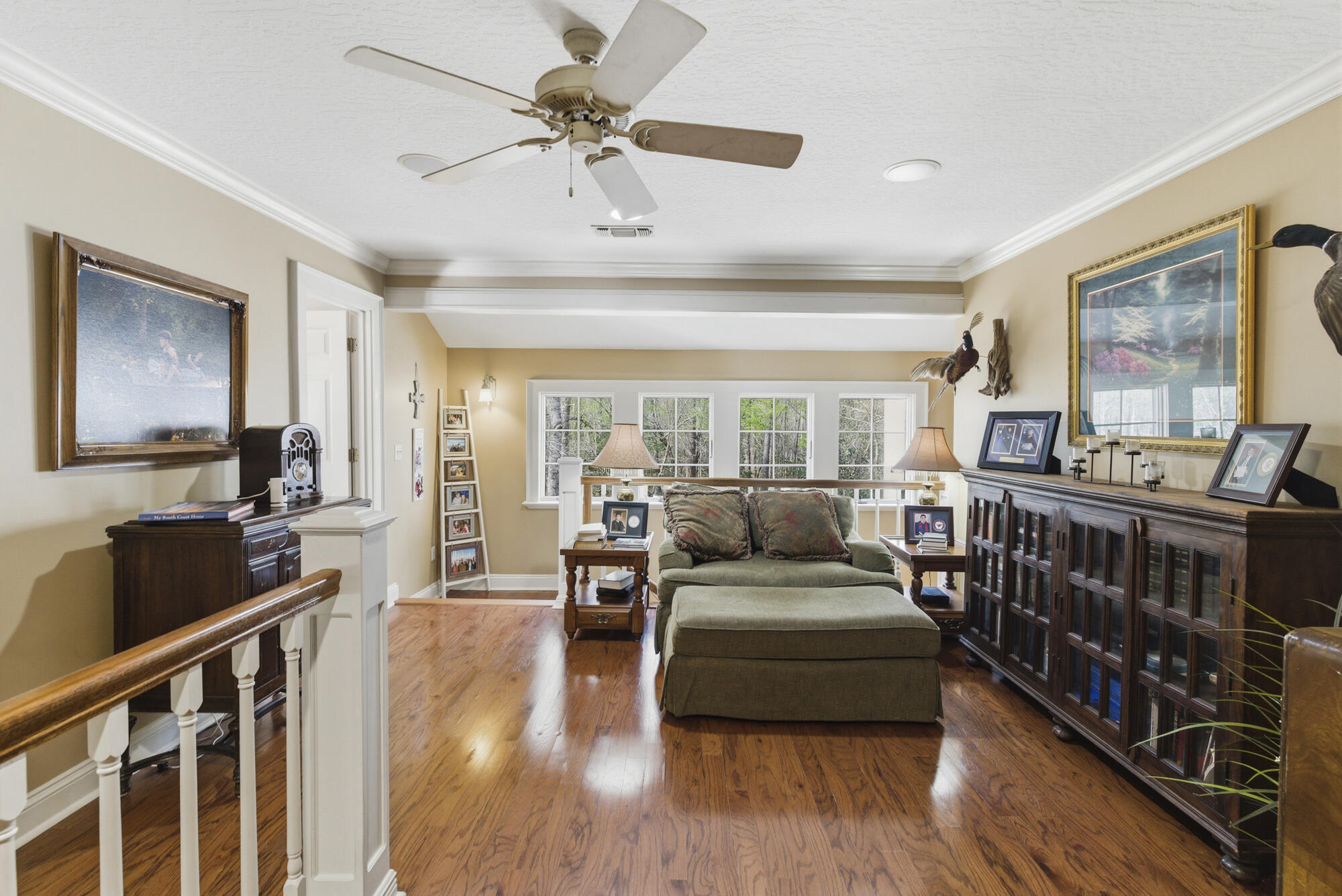 Living room with green sectional, polished wood floors, and broad windows overlooking trees.