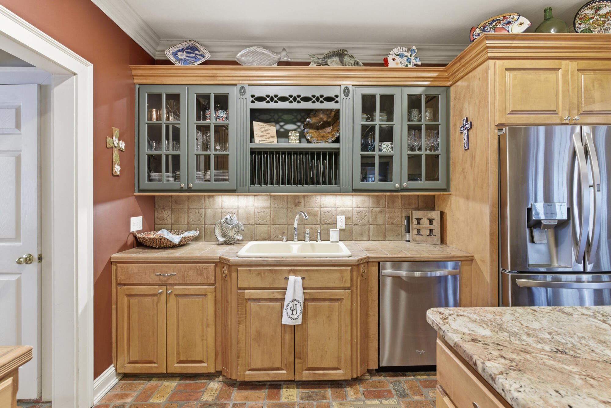 Kitchen with wood and sage-green cabinetry, tiled floors, and stainless steel appliances.
