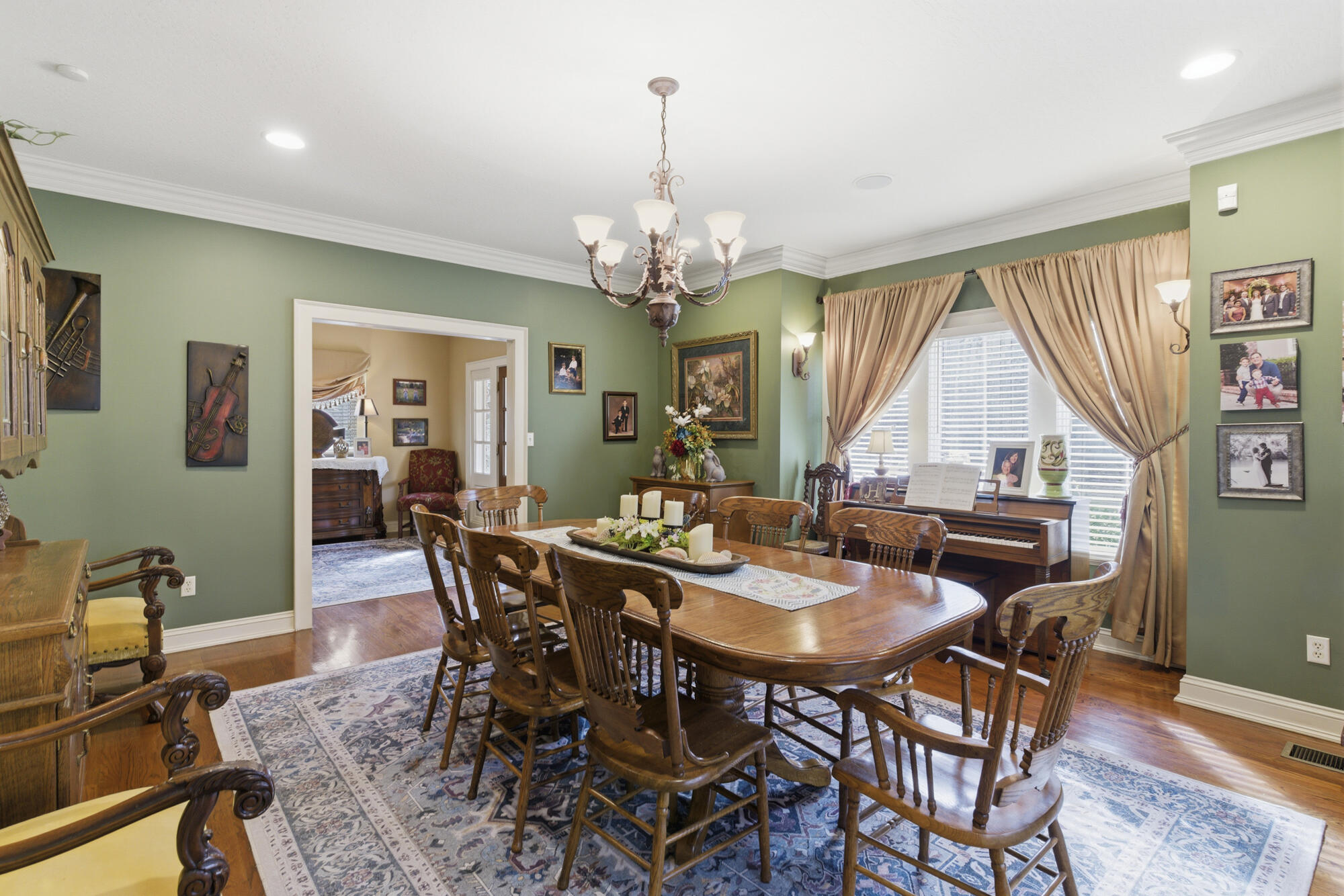 Dining room with a large wooden table, patterned rug, piano, and sage-green walls.