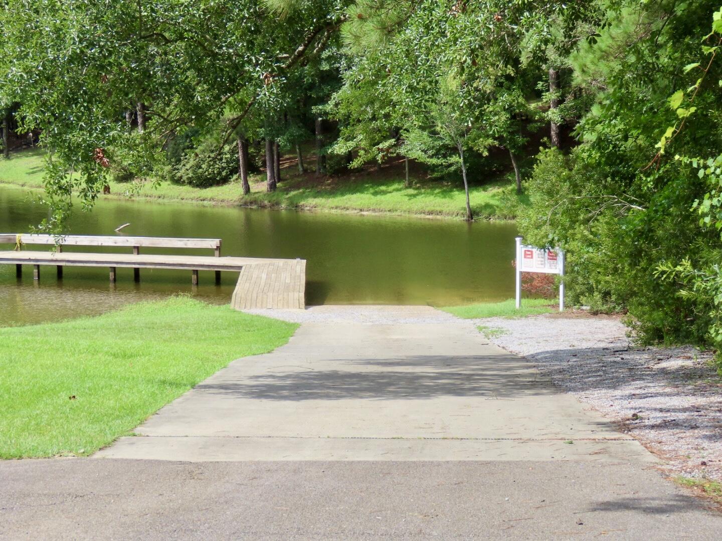 Tree-lined pond with a wooden dock and paved path to the water.