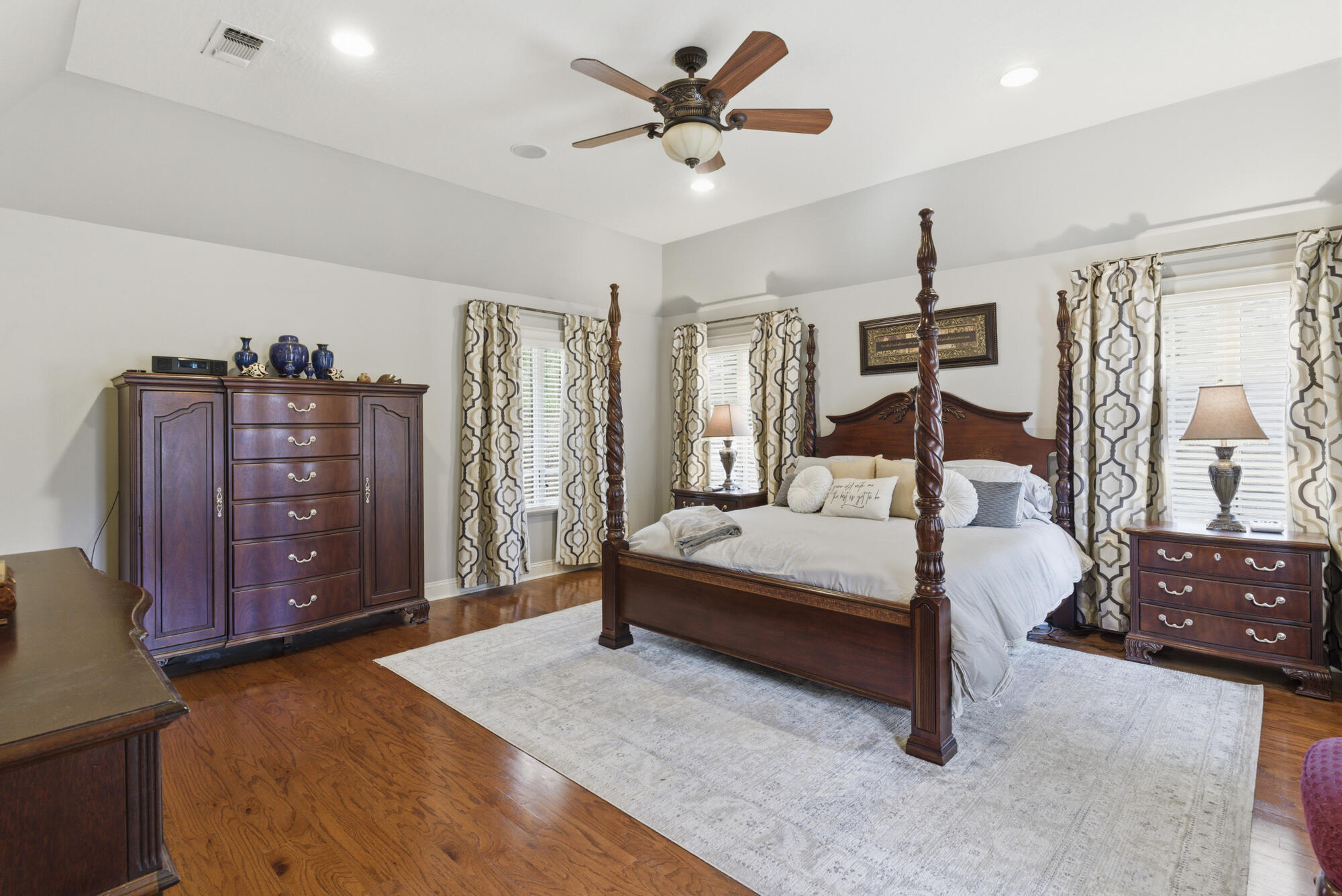 Bedroom with a dark wood four-poster bed, matching furniture, patterned curtains, and hardwood floors.