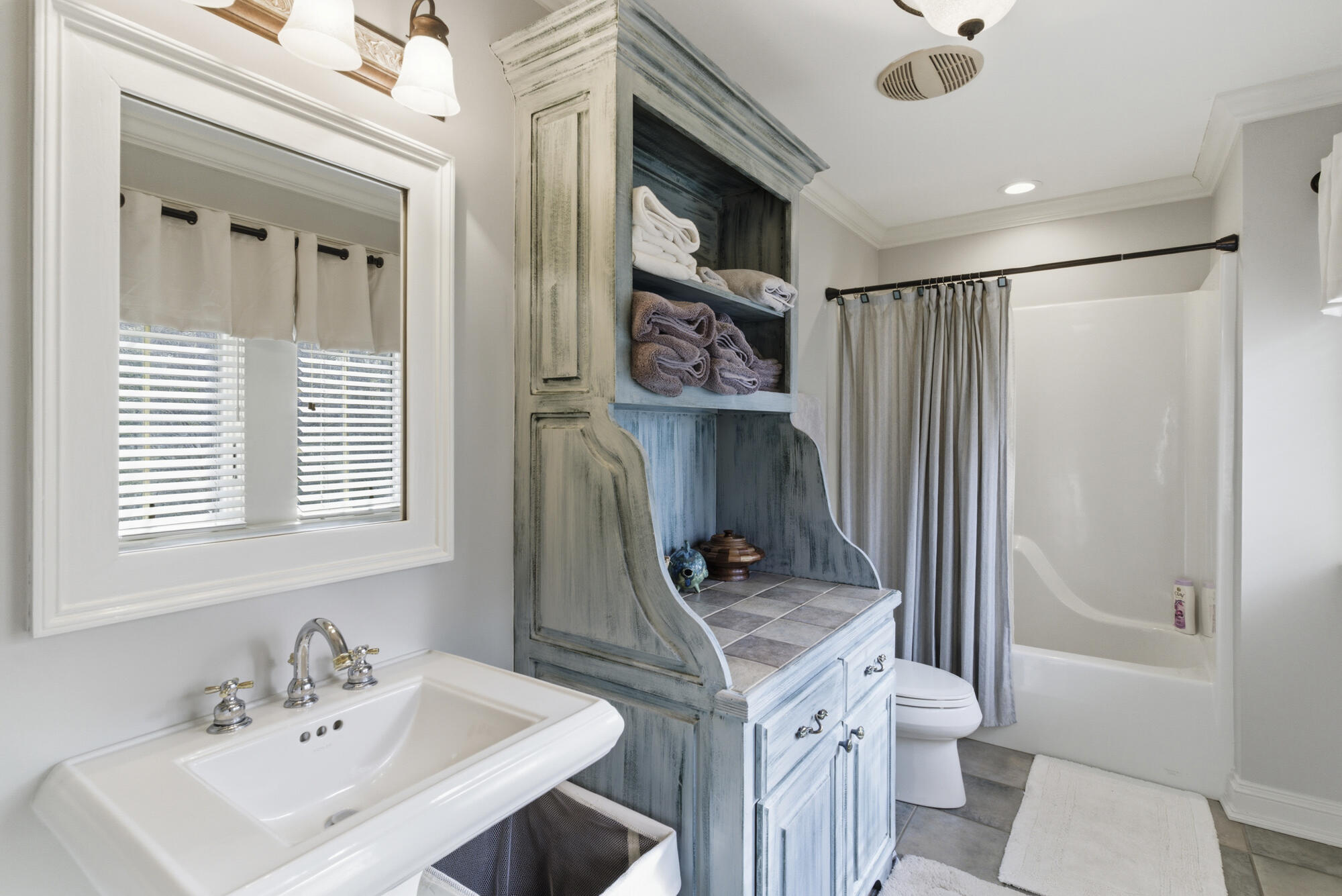Bathroom with distressed blue built-in vanity, open towel shelves, and a tub behind a gray curtain.