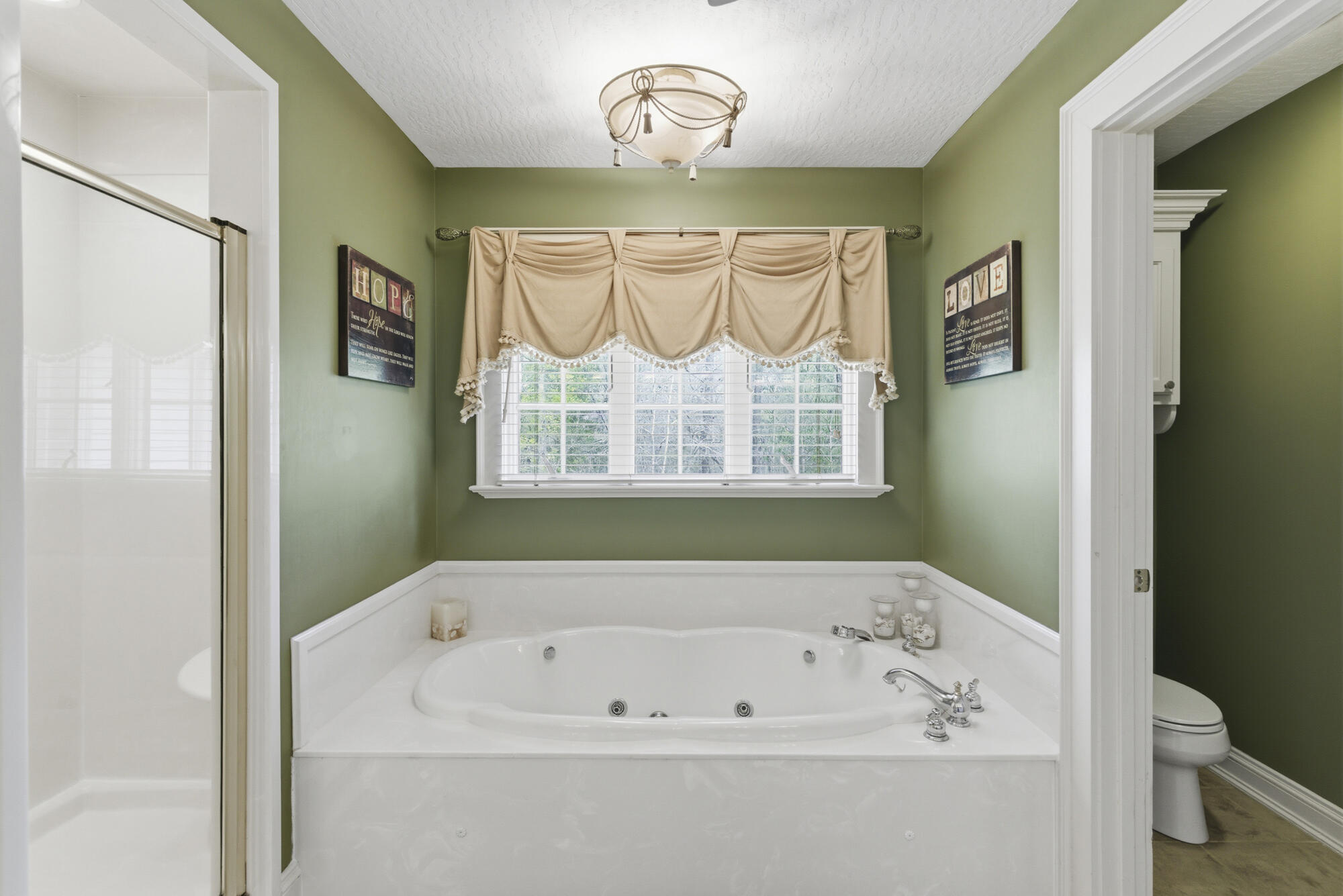 Bathroom with a large jetted tub beneath a curtained window and a glass shower beside it.