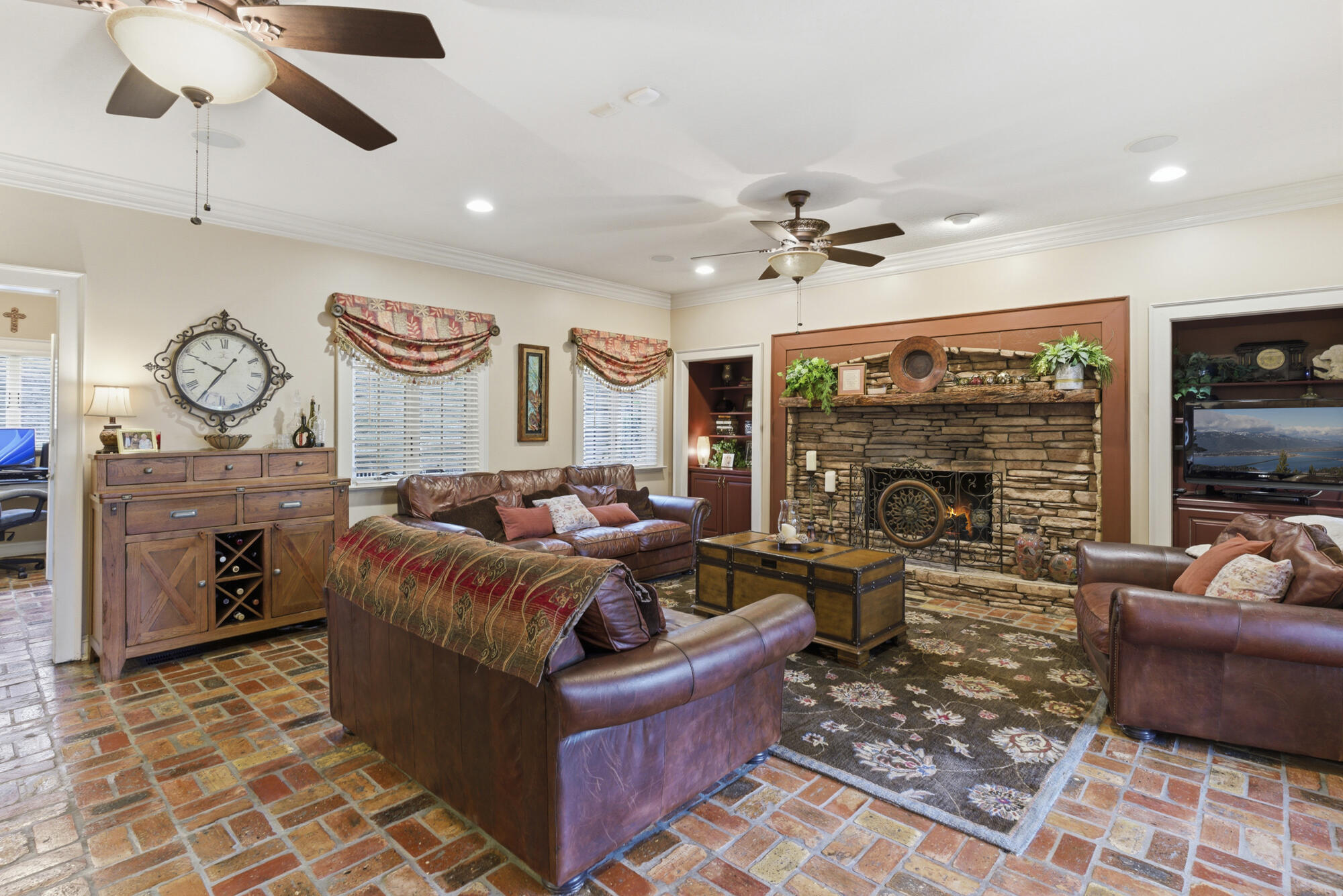 Living room with a stone fireplace, leather seating, and brick tile flooring.