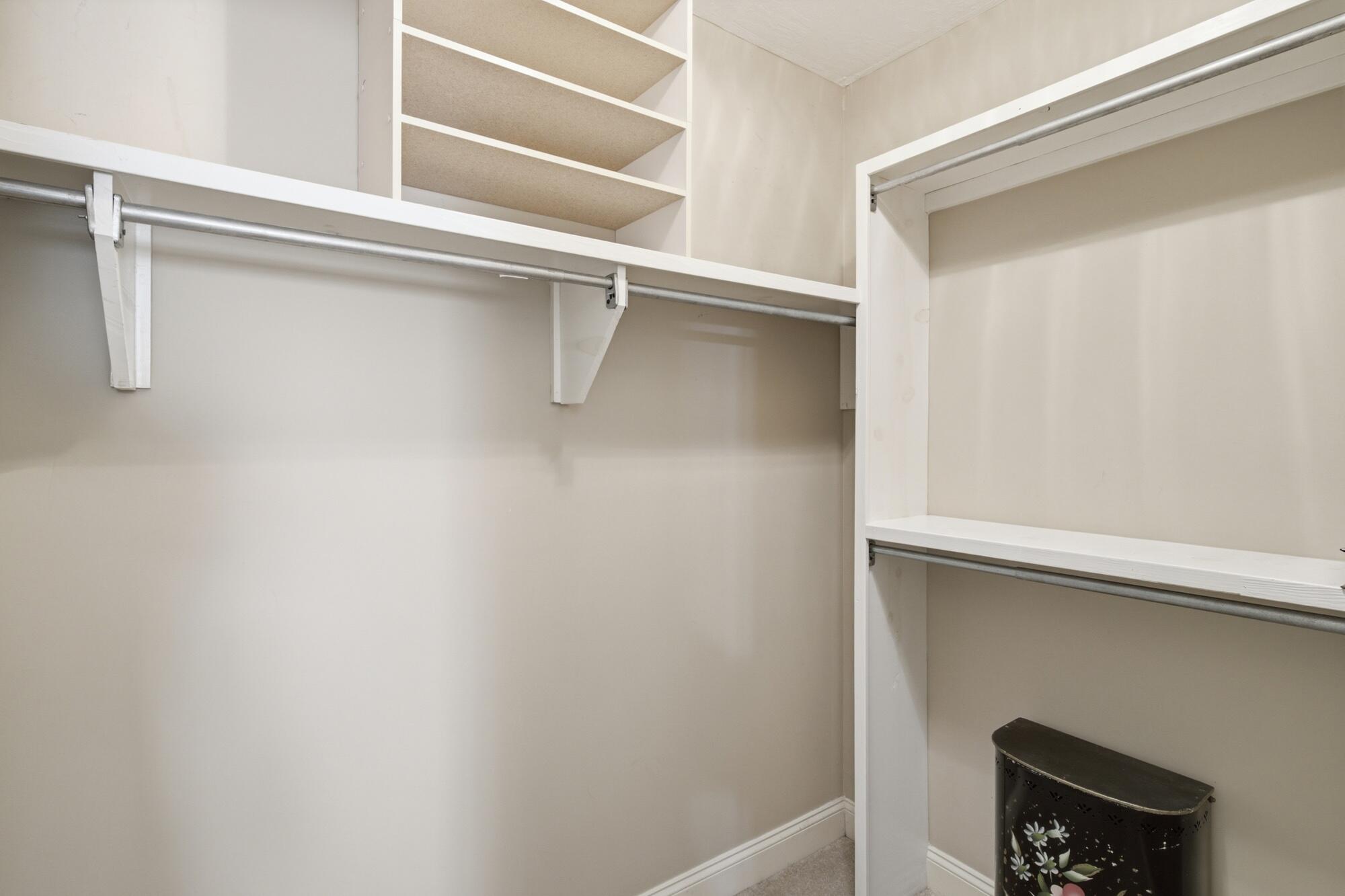 Walk-in closet with built-in white shelves and hanging rods beside a small floral cabinet.