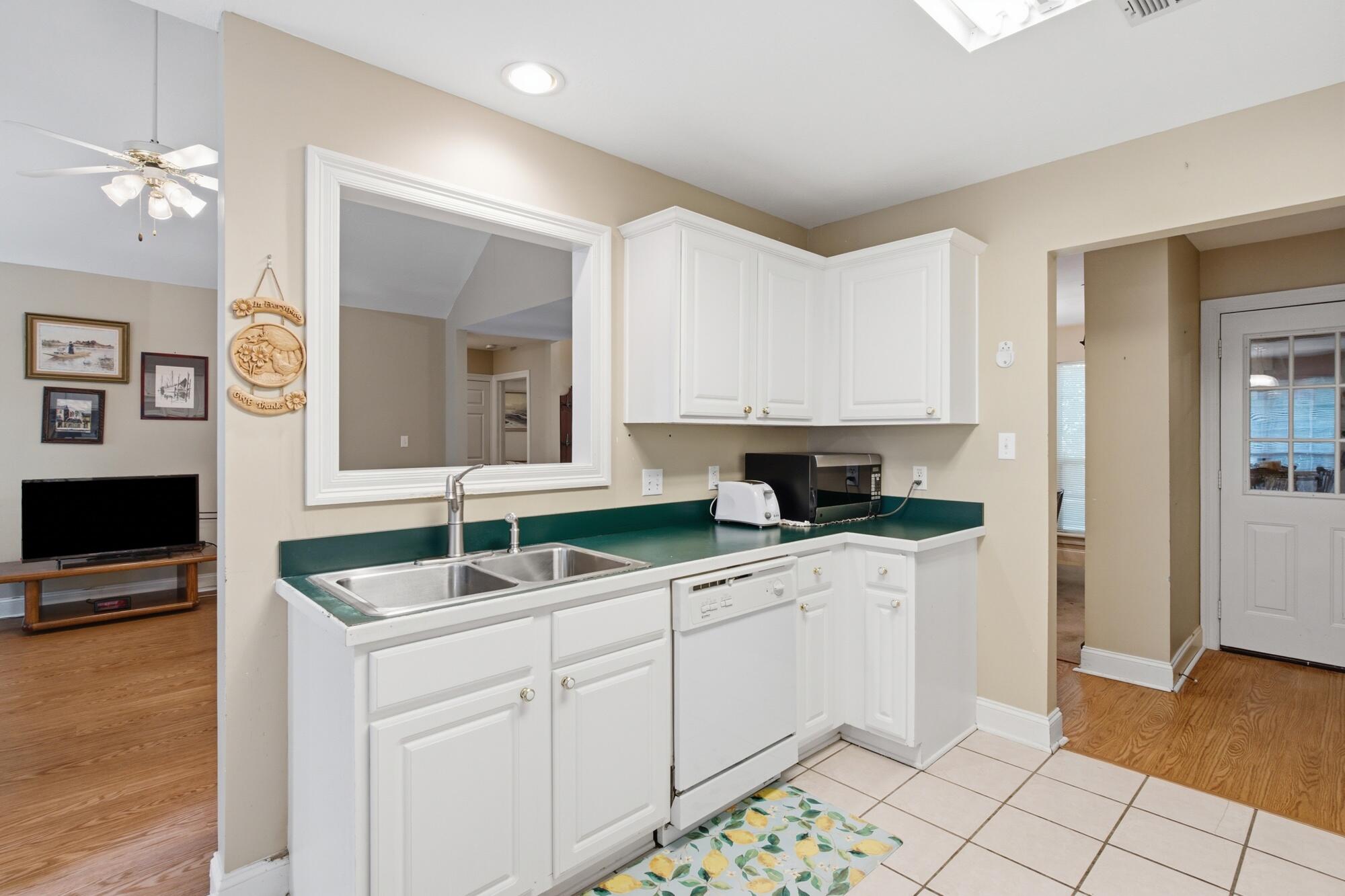 Kitchen with white cabinets, green countertops, a double sink, and a pass-through to the living area.