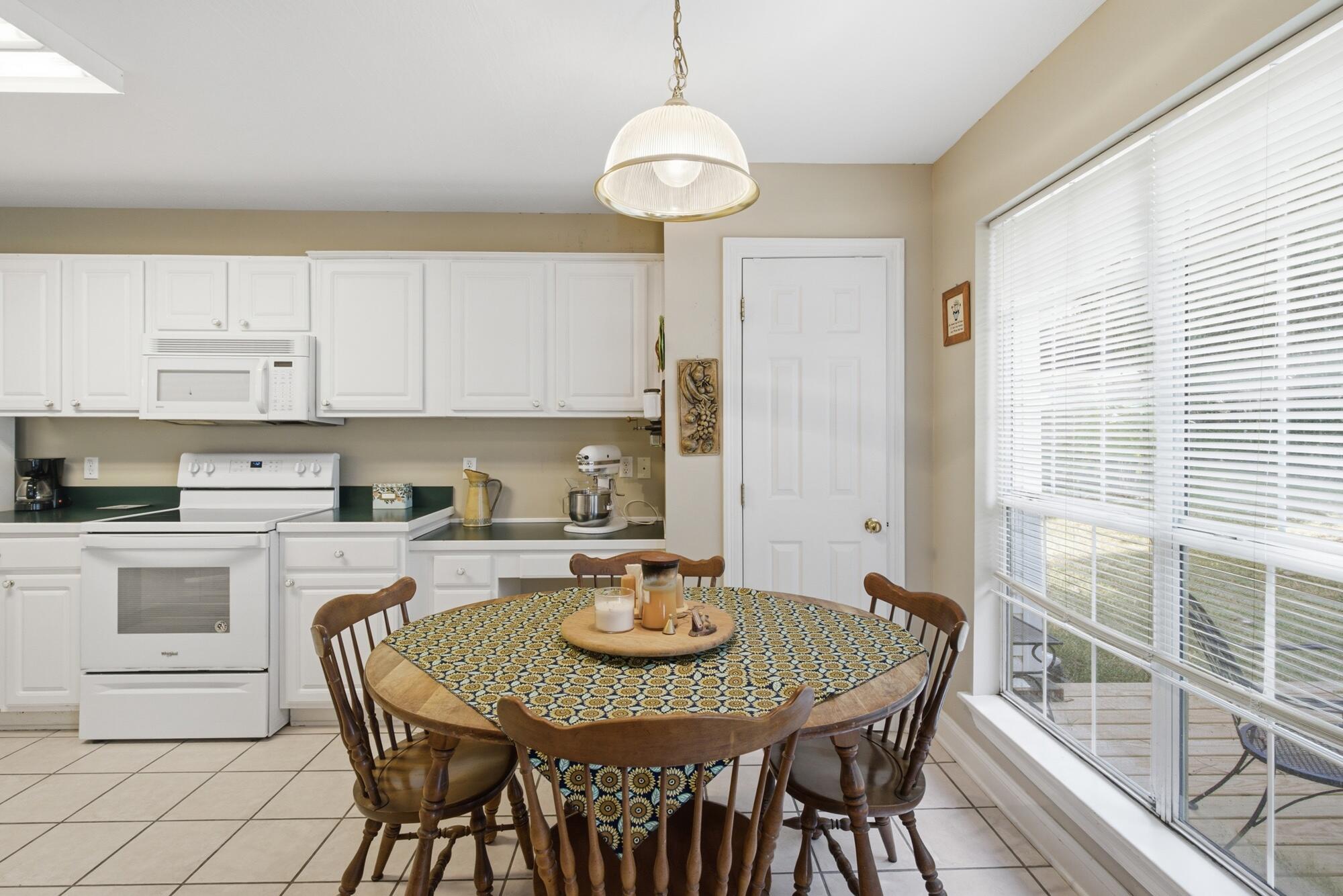 Kitchen with white cabinets and appliances, a round dining table, and a large window overlooking a deck.
