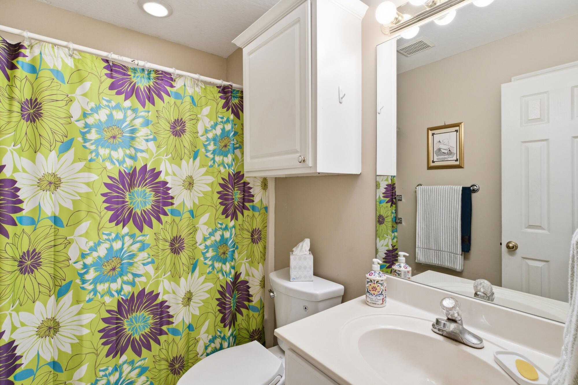Bathroom with a bright floral shower curtain, white vanity, and mirrored cabinet.