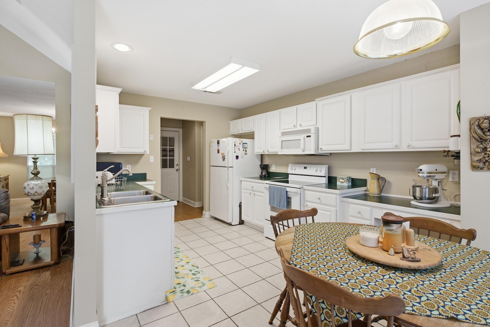 Kitchen with white cabinets, green countertops, and a round dining table beside the tiled floor.